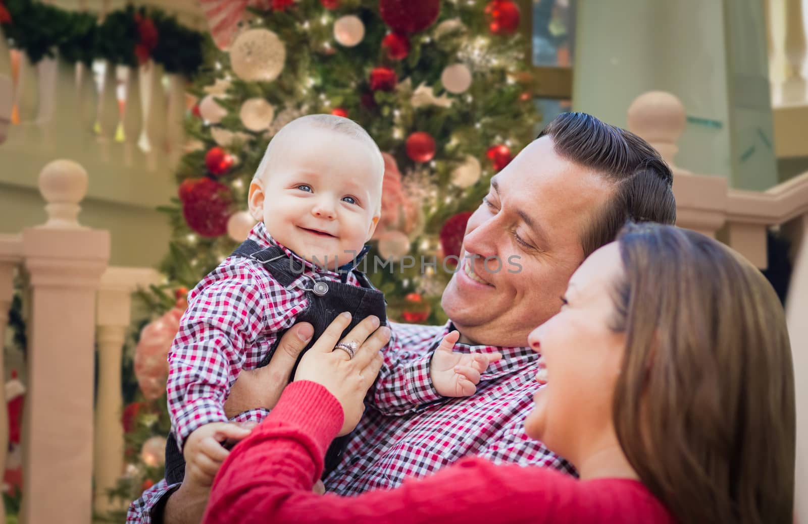 Happy Young Parents with Baby In Front of Decorated Christmas Tree. by Feverpitched