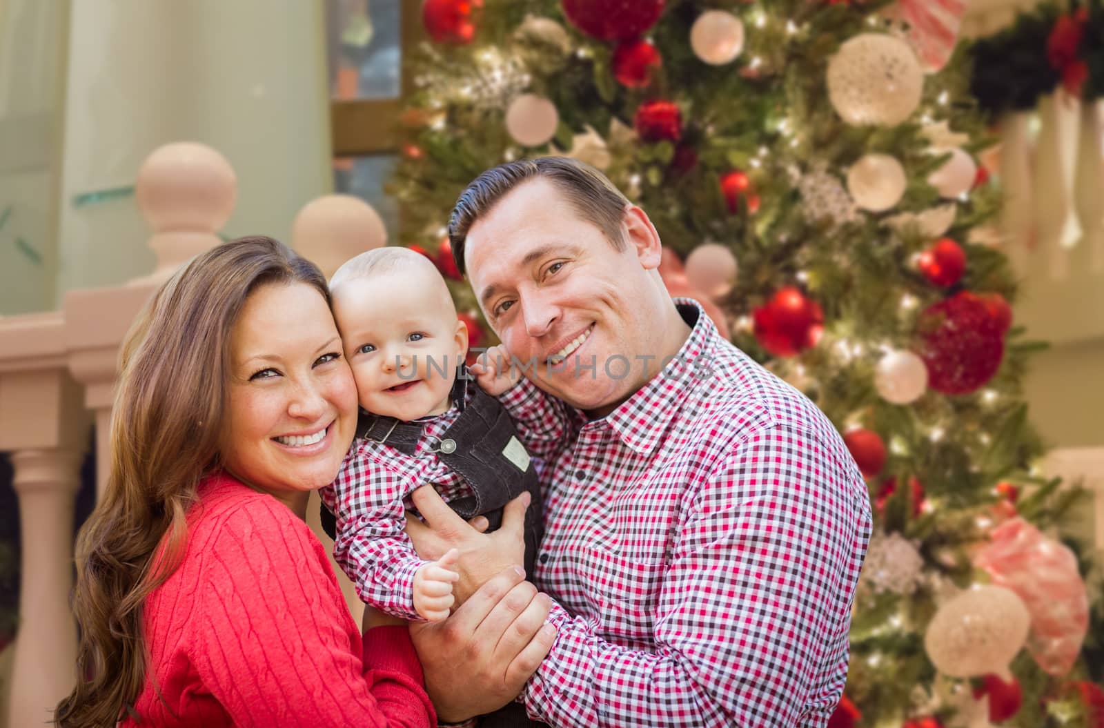 Happy Young Parents with Baby In Front of Decorated Christmas Tree.