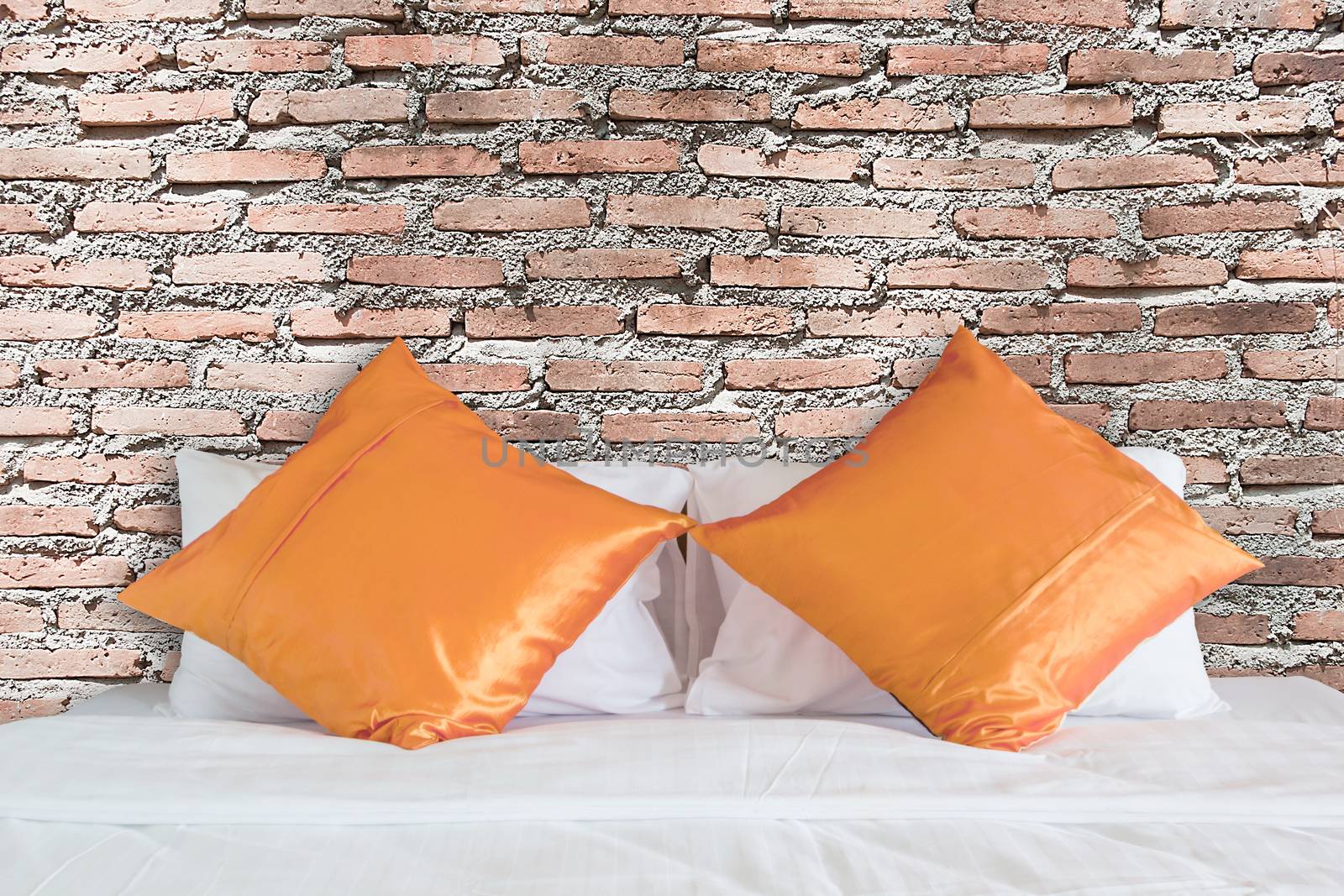 vintage red brick wall and orange pillow on white bed by rakoptonLPN