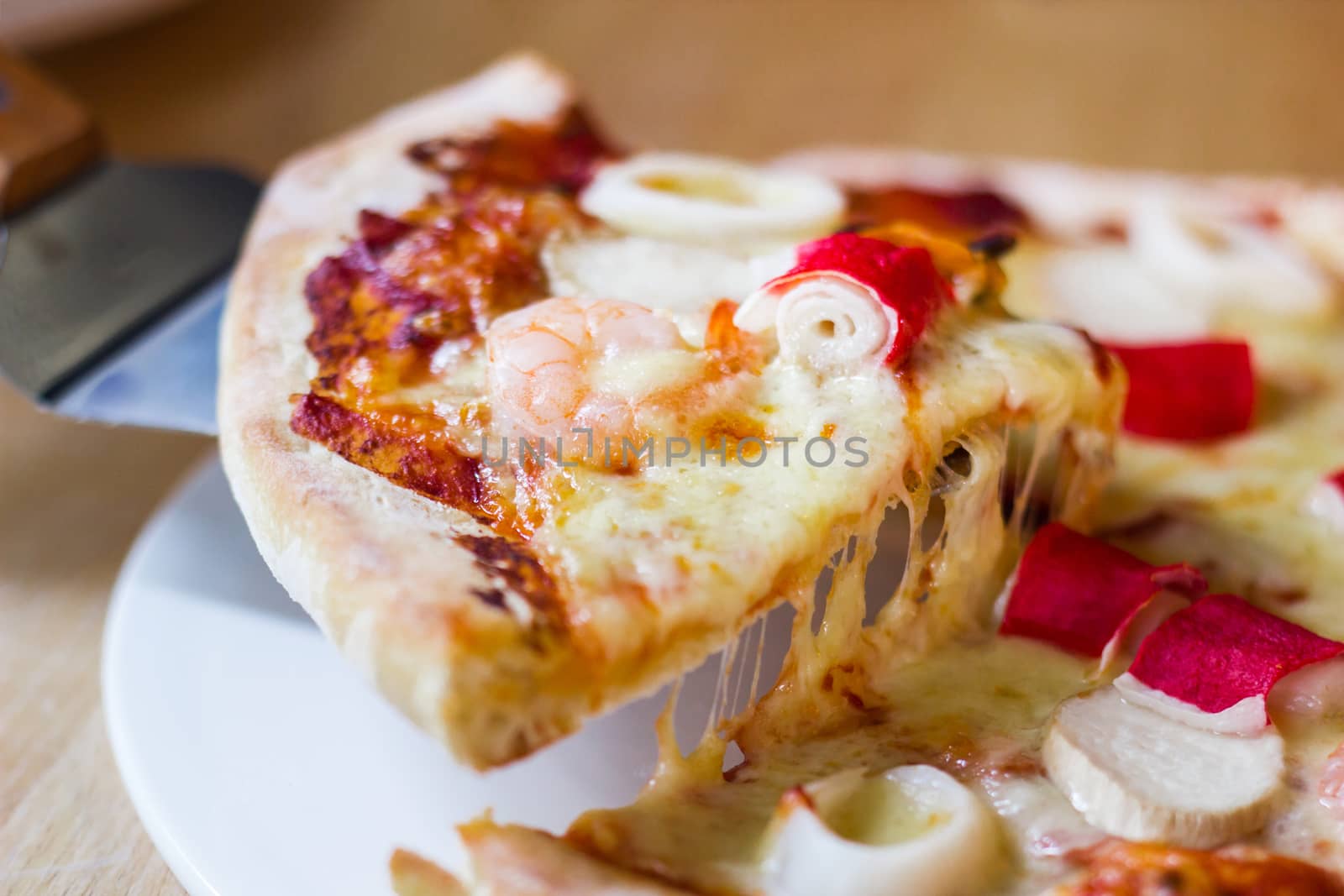Hot seafood pizza slice with melting cheese on rustic wooden table.