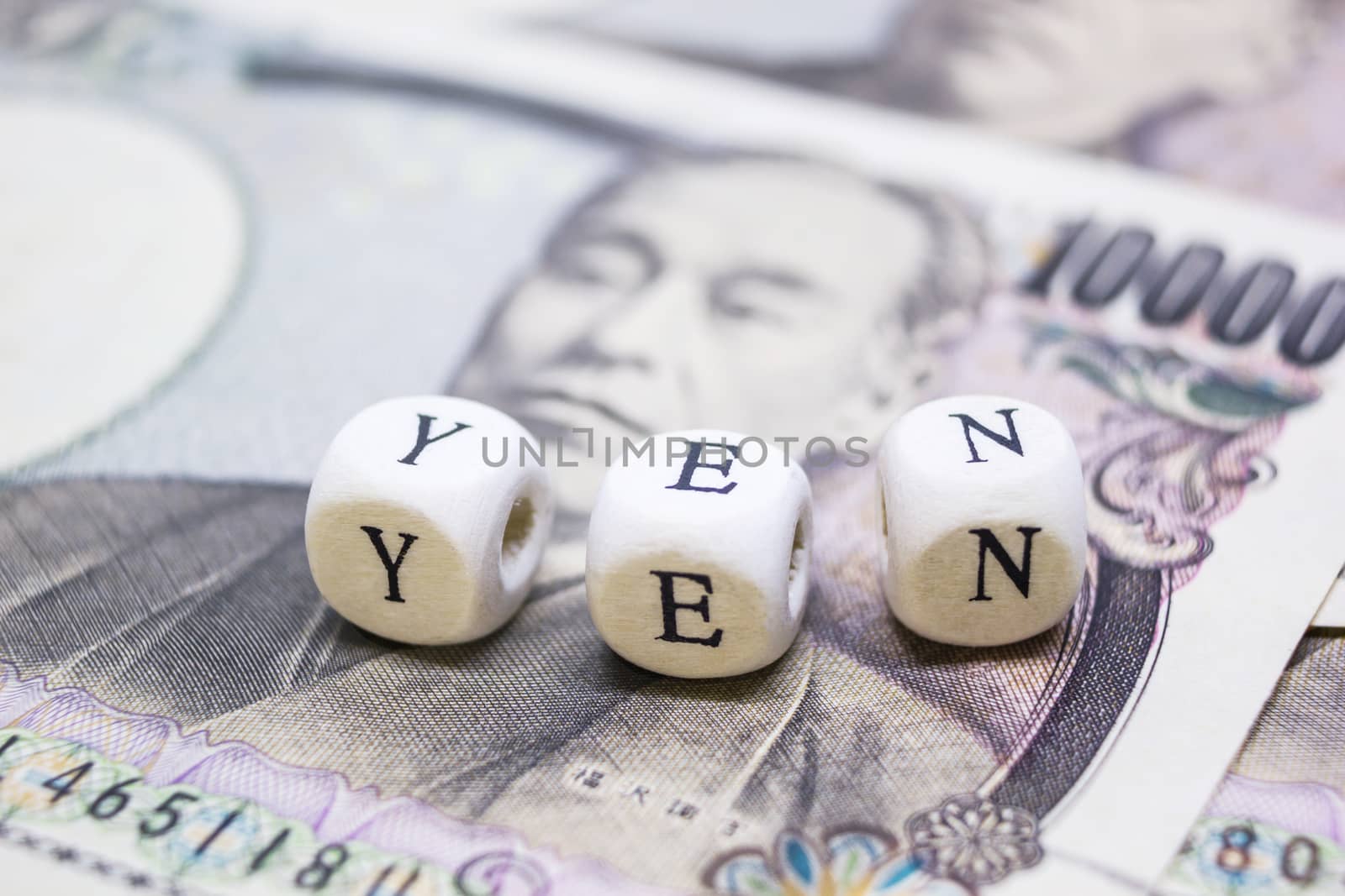 close-up of wooden cube with text "Y E N" on banknote YEN for business and financial concept.
