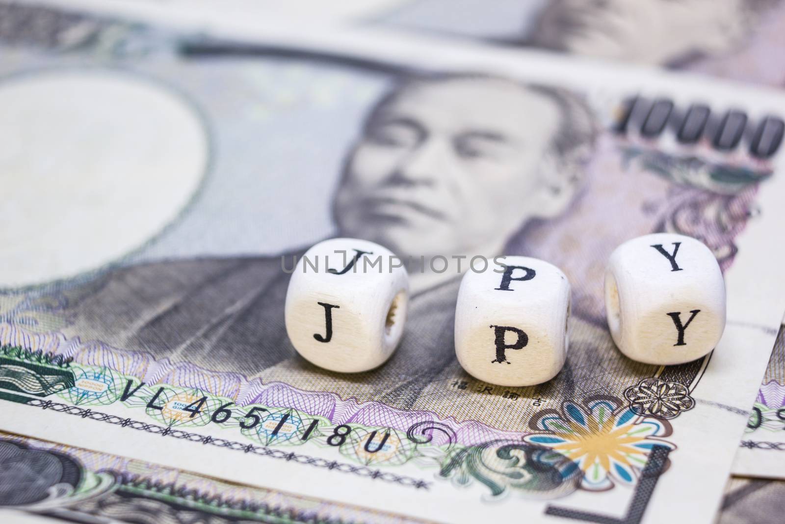 close-up of wooden cube with text "J P Y" on banknote YEN for business and financial concept.