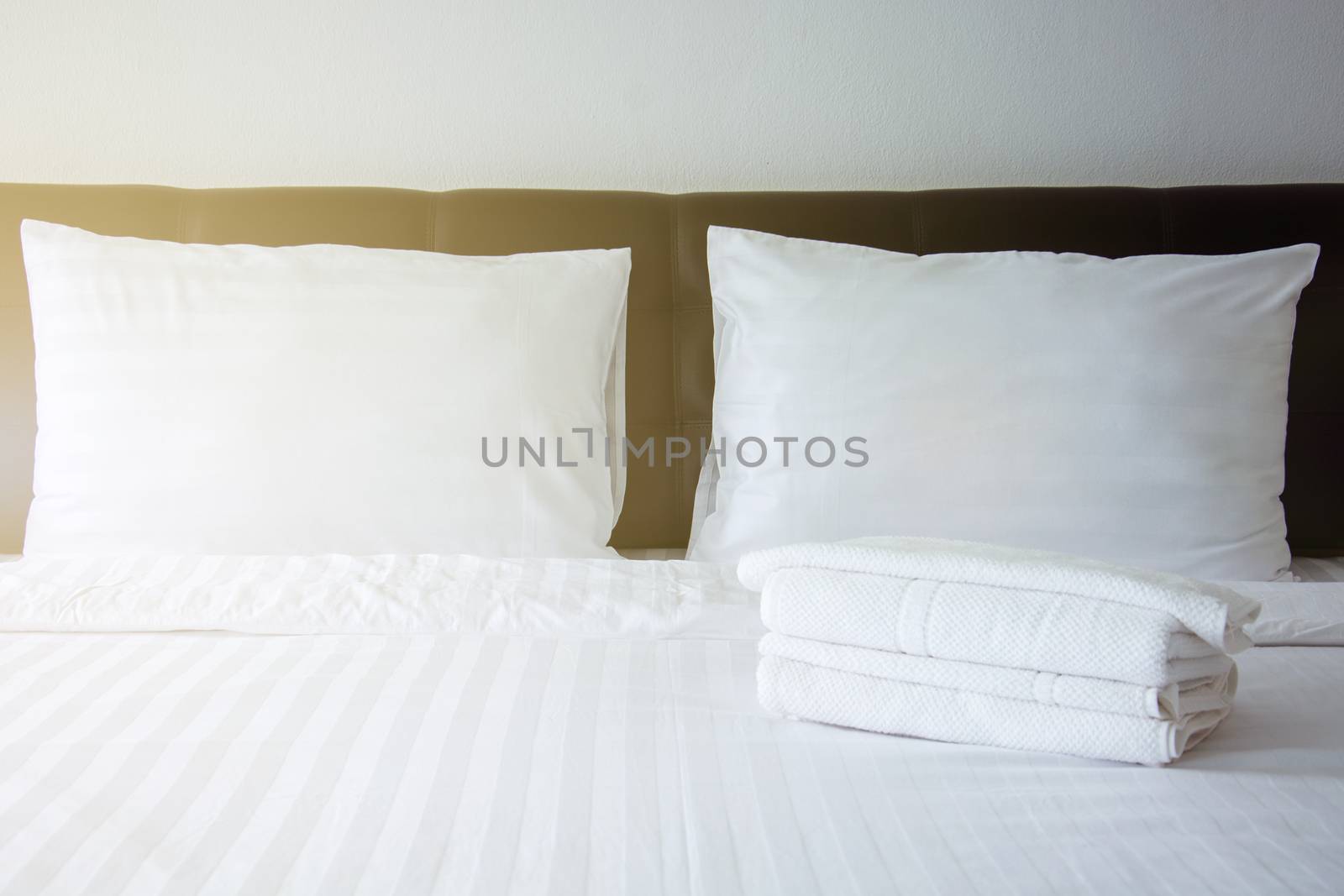 white pillow, white blanket and white towel on bed in bedroom with lighting upper left side