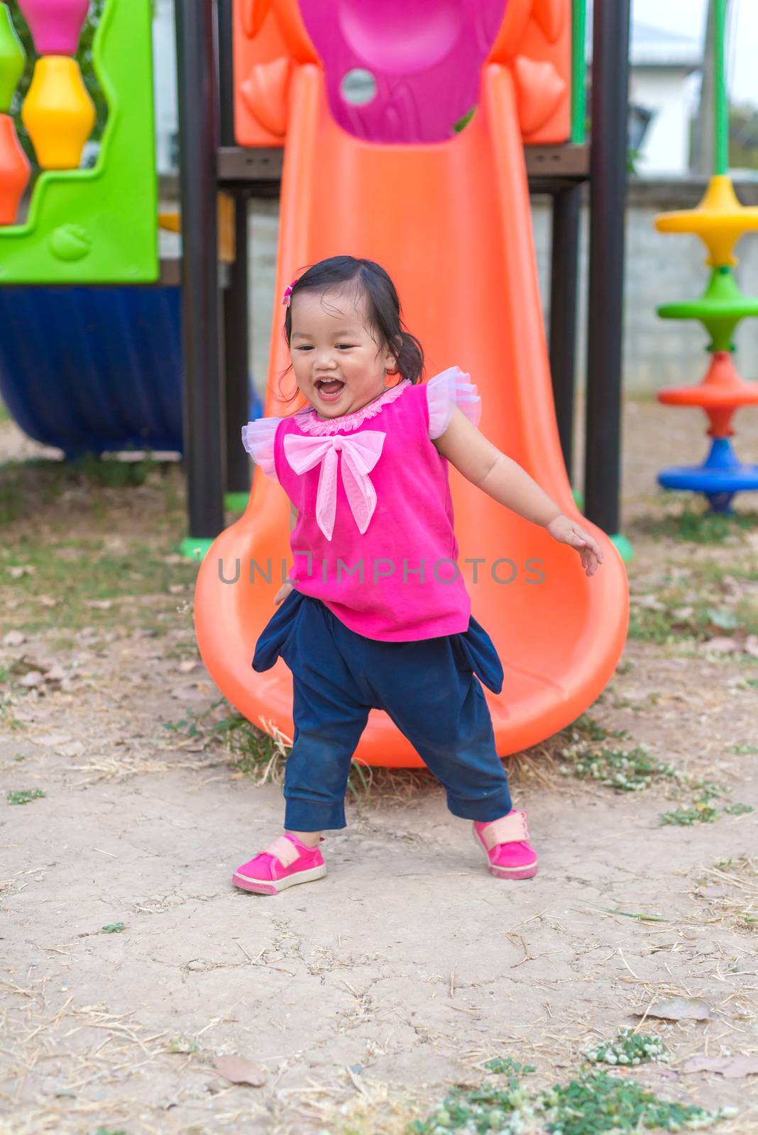 Toddler girl playing on a slide at children playground.