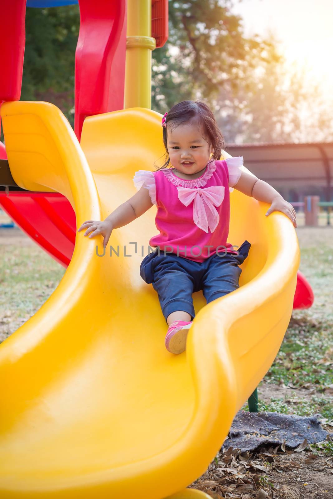 Toddler girl playing on a slide at children playground.