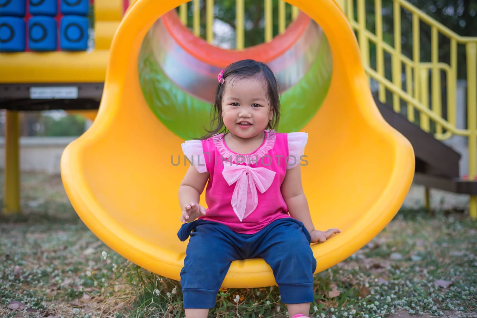 Toddler girl playing on a slide at children playground.