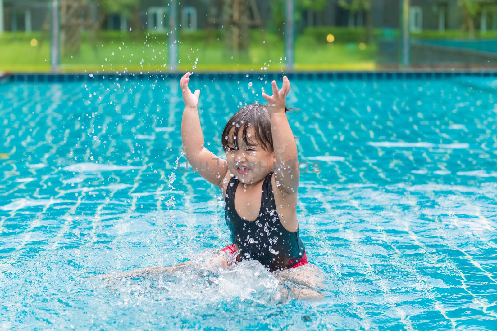 Cute girl or little child playing in swimming pool happily.