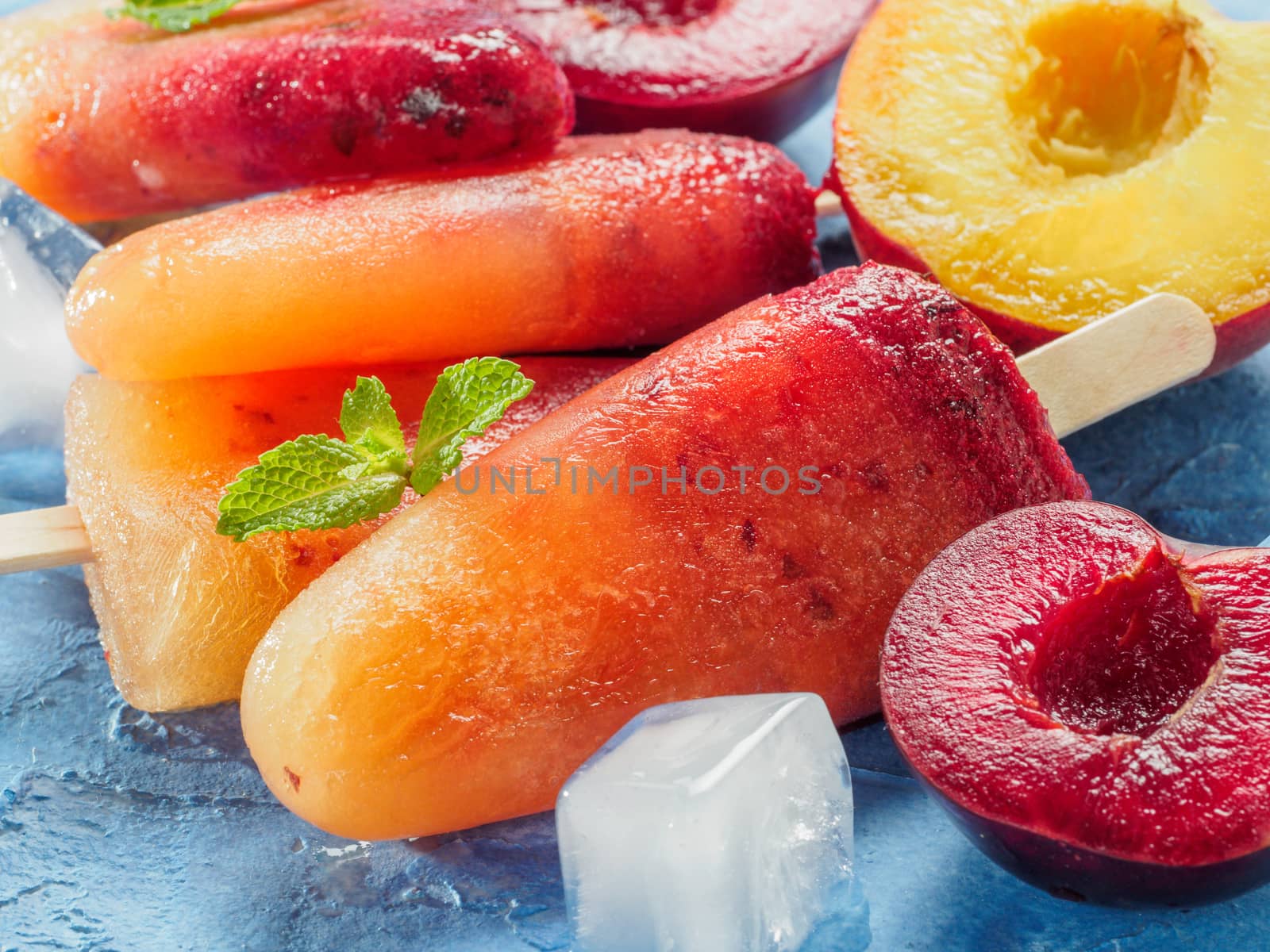 Close up view of plum and peach popsicle on blue concrete background. Fruit popsicles ice cream with fresh plums and peach. Copy space.