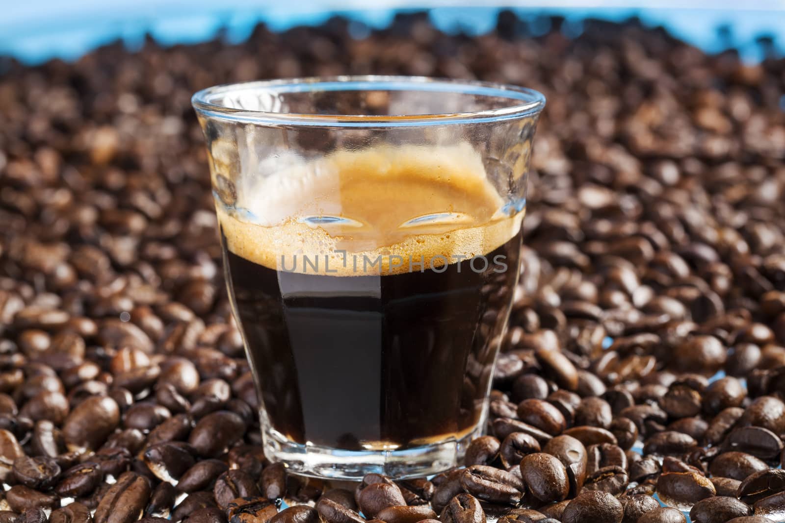 Glass with double espresso surrounded by coffee beans