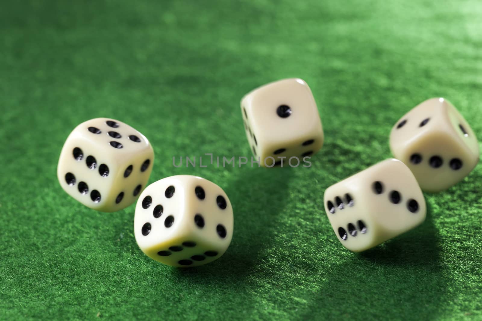 Five rolling dices in motion on green felt