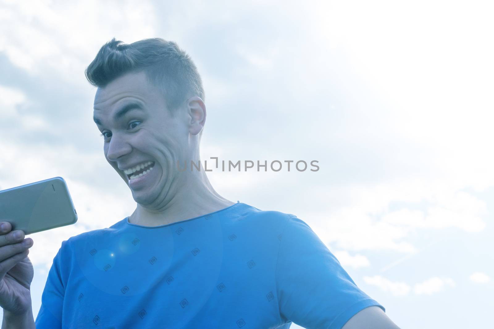 A young man emotionally looks at the phone. Nature, summer, portrait.