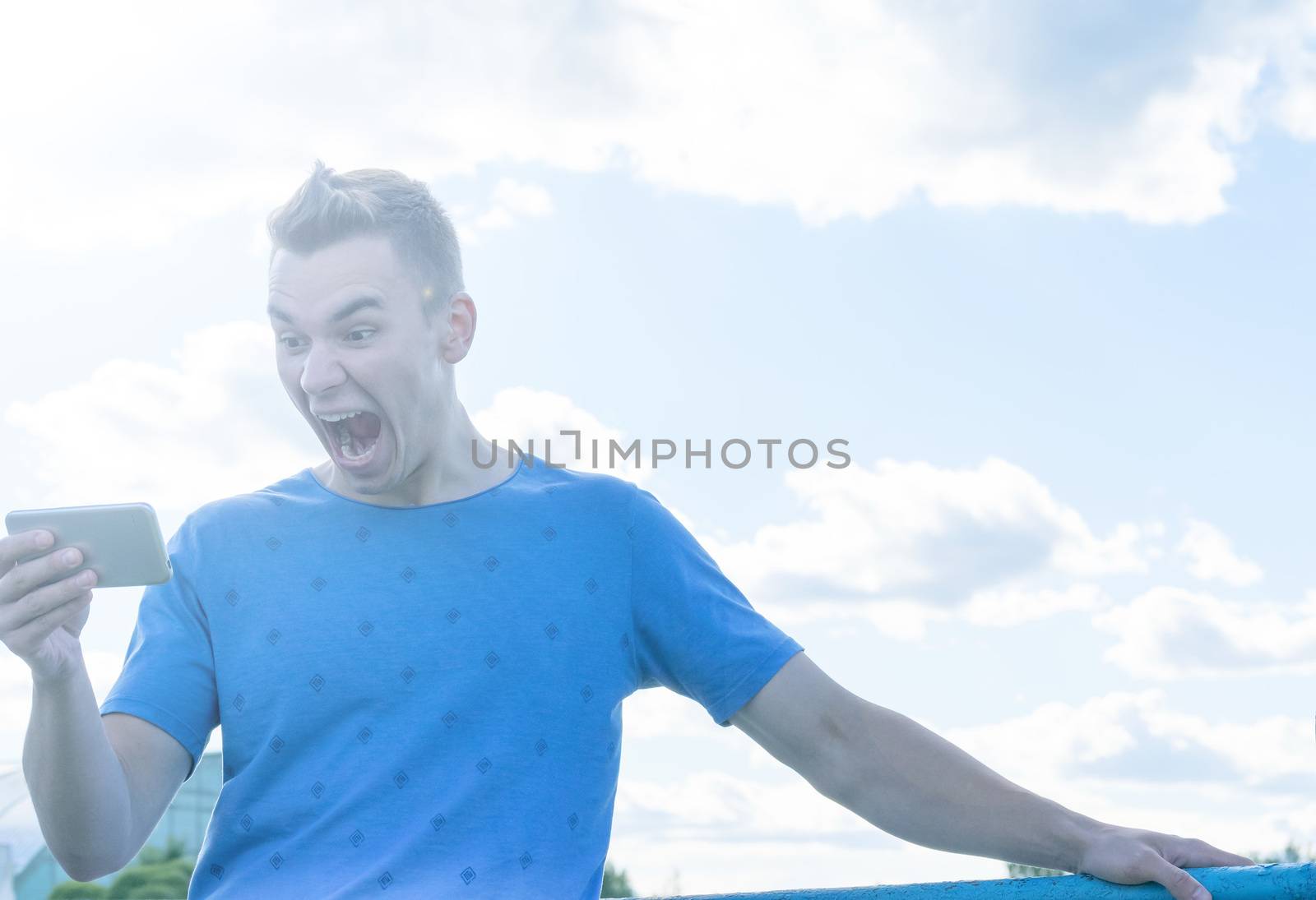 A young man emotionally looks at the phone. Nature, summer, portrait.