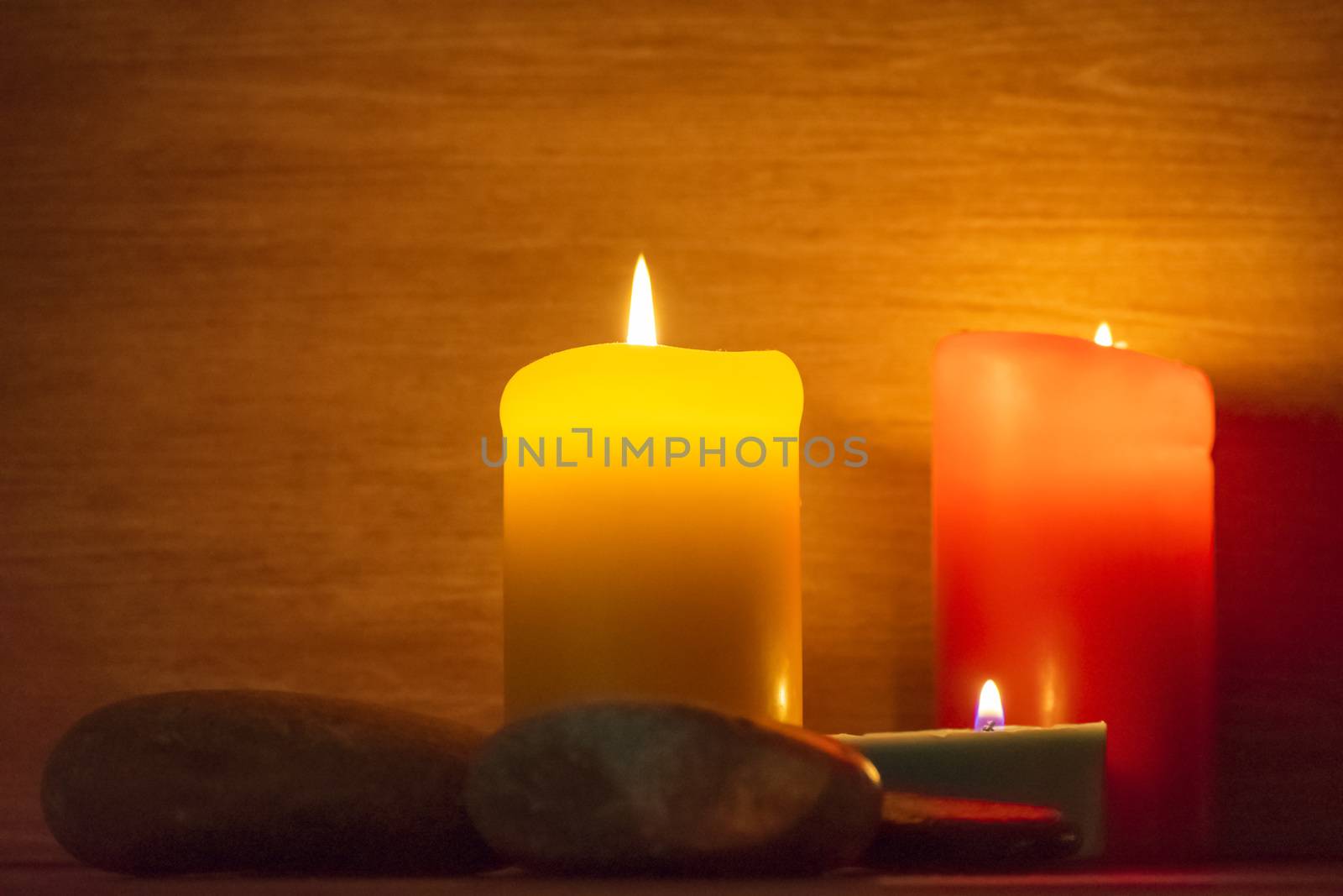 Several multi-colored candles are lit and surrounded by stones.