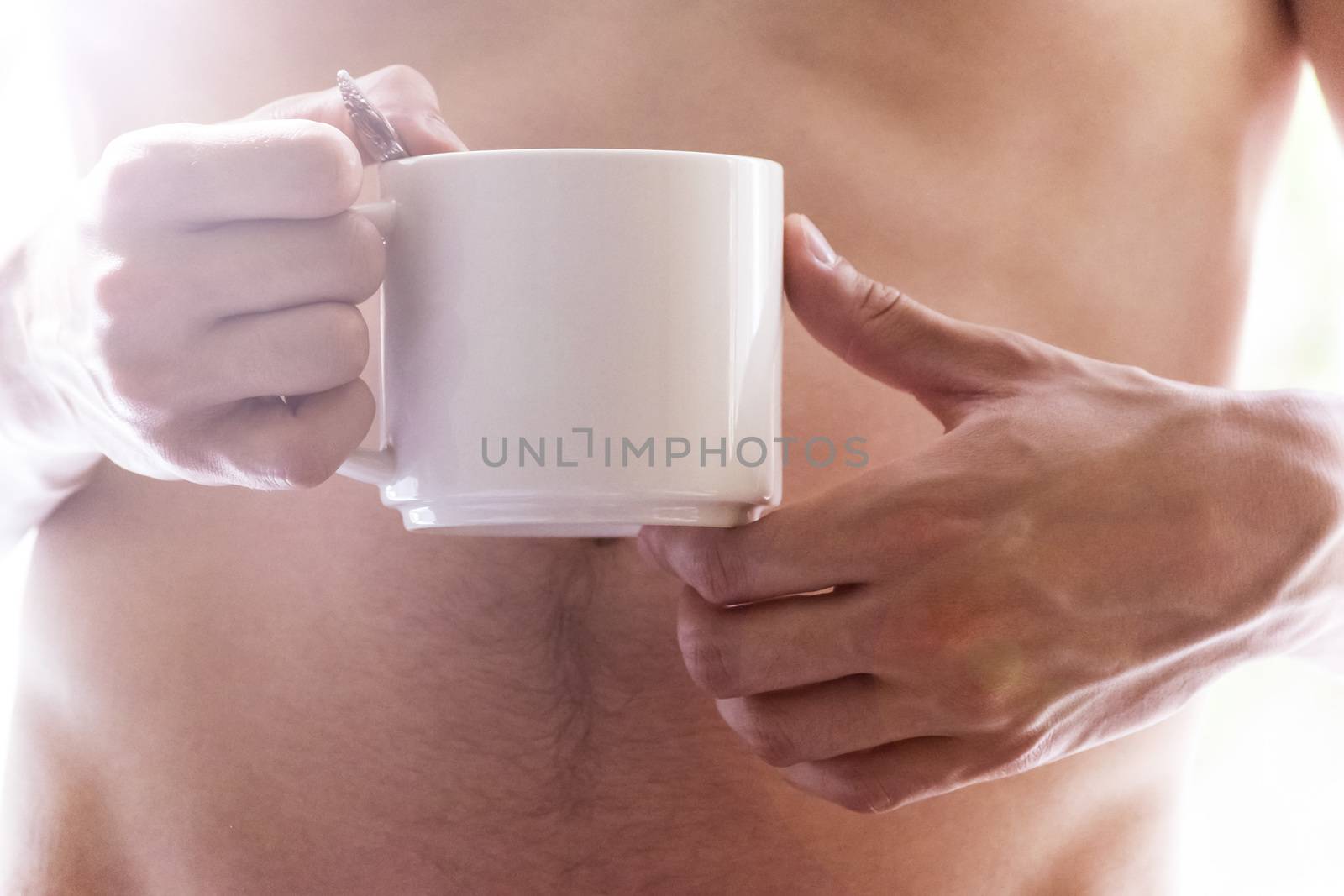 A young man holding a mug in his hands. Morning, summer, autumn, bare-chested. Tea, coffee.