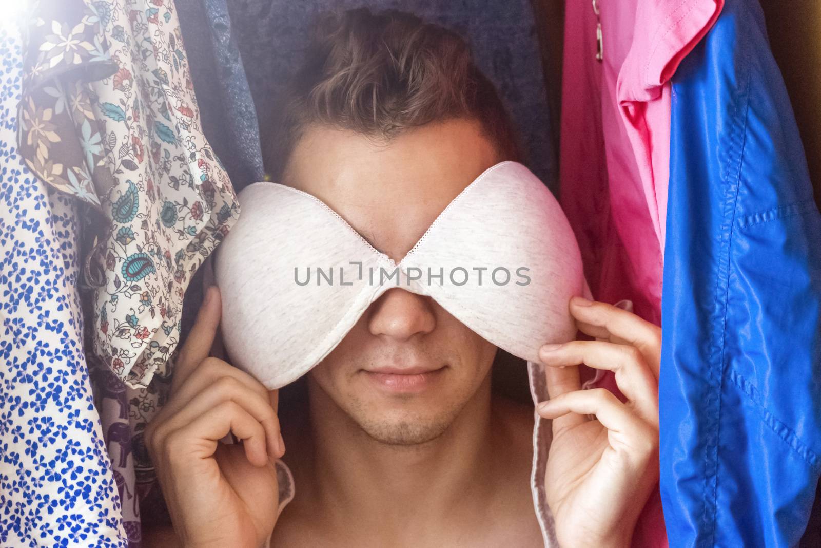 A young man hiding in the closet among women's clothing. Lover in the closet.