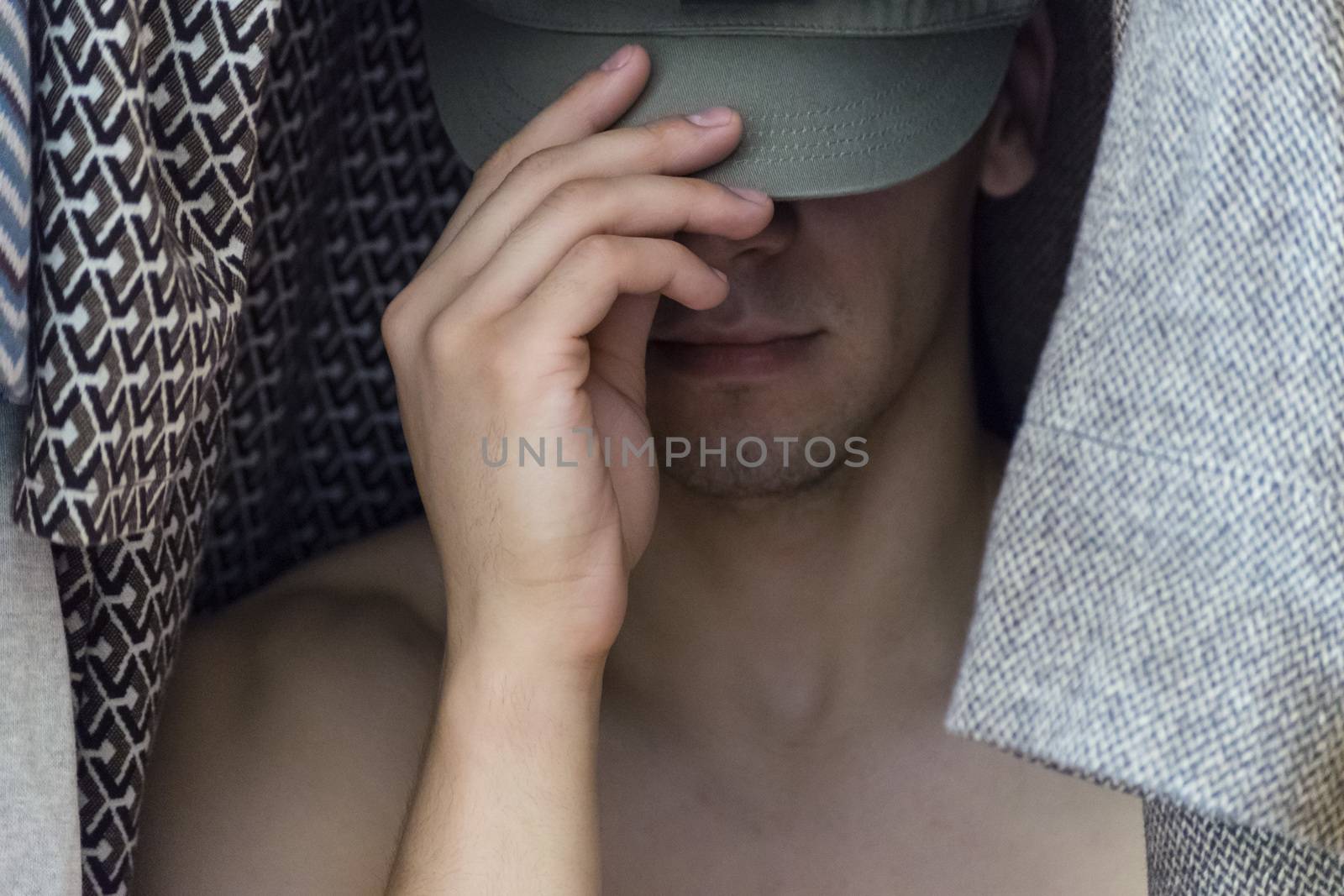The young man covers his face with hat sitting in the closet women's clothing