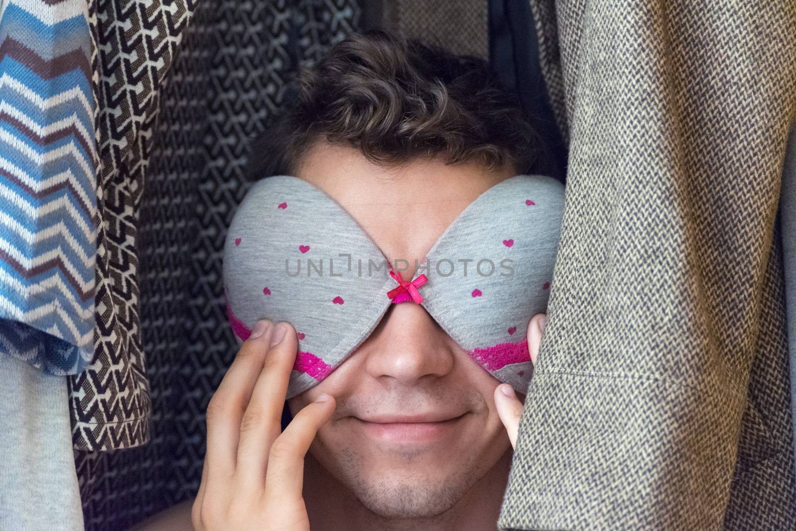 A young man in the closet with a bra on his face.