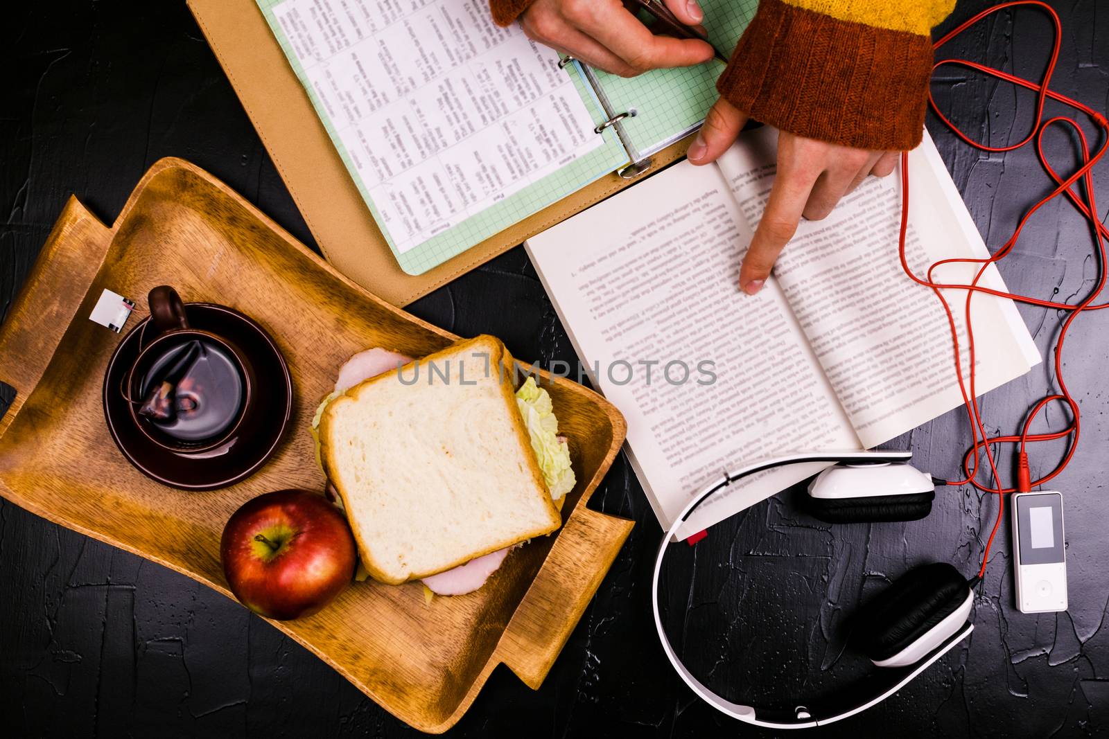 A man reads, translates the text. Sandwich, headphones, pencils, notebooks. Still life, black background.