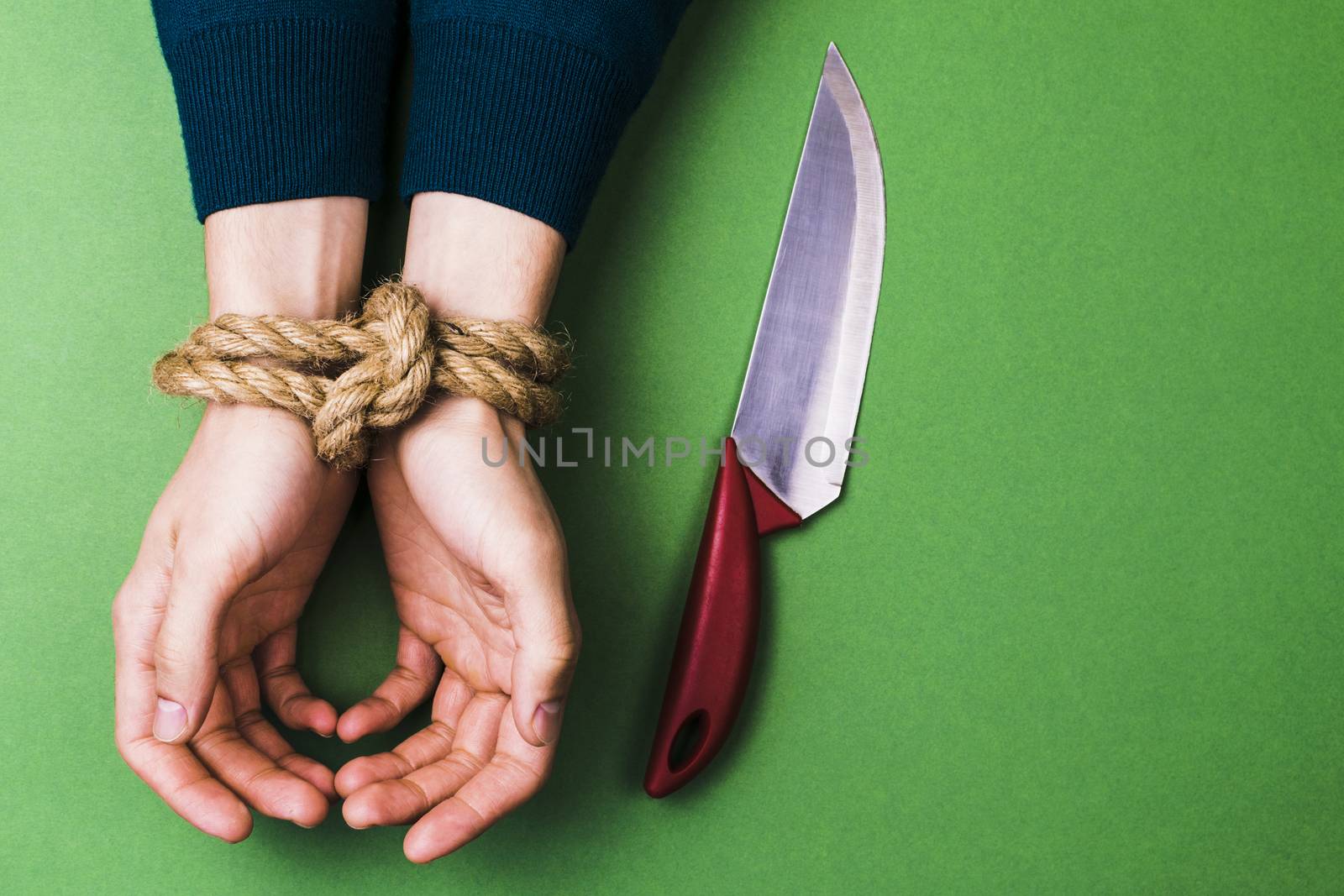 The man with bound hands and knife on green background