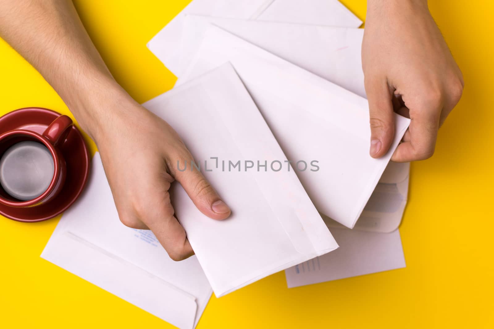 A man sorts the mail. Male hands the envelopes on a yellow background, a red coffee Cup.