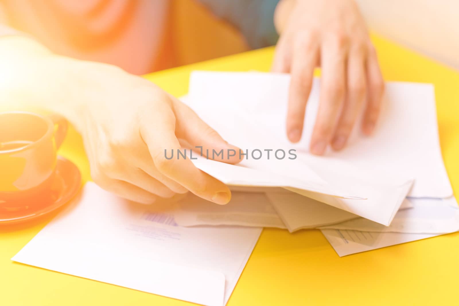 A man sorts the mail. Male hands the envelopes on a yellow background, a red coffee Cup.