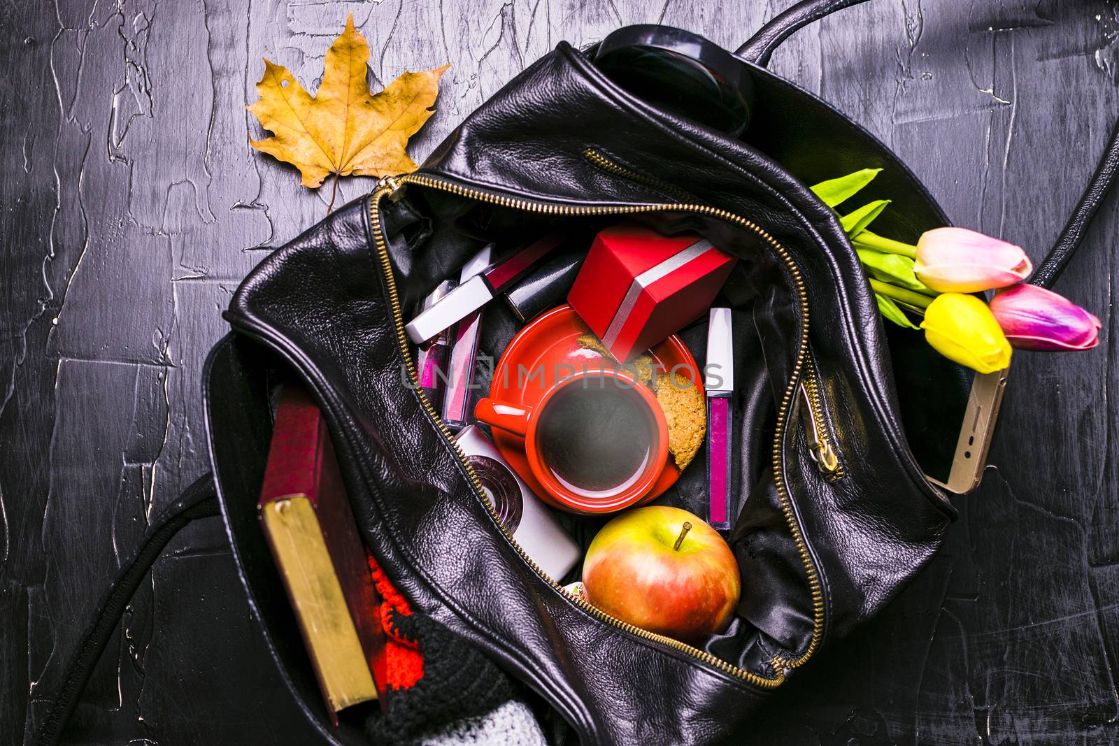 The contents of the female handbag. Flowers, lipstick, camera, coffee, biscuits, beads. Dark background.