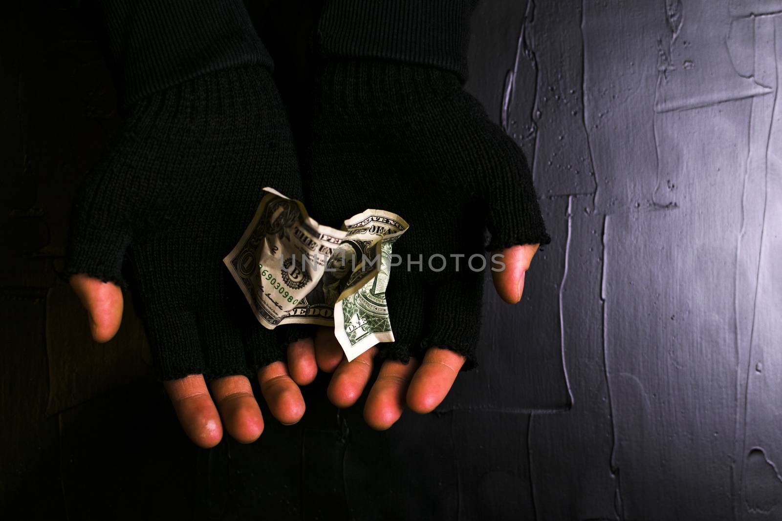 Man in black gloves holding a dollar bill on a black background.