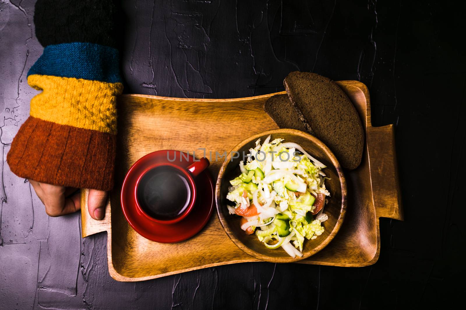 Man holding wooden tray with a salad and coffee on a black background