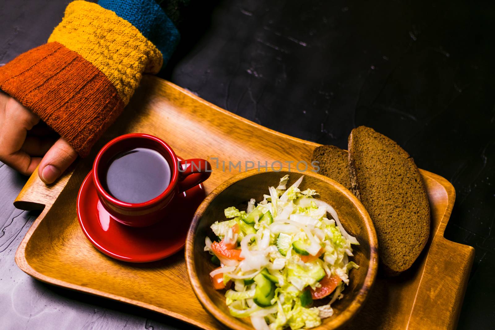 Man holding wooden tray with a salad and coffee on a black background