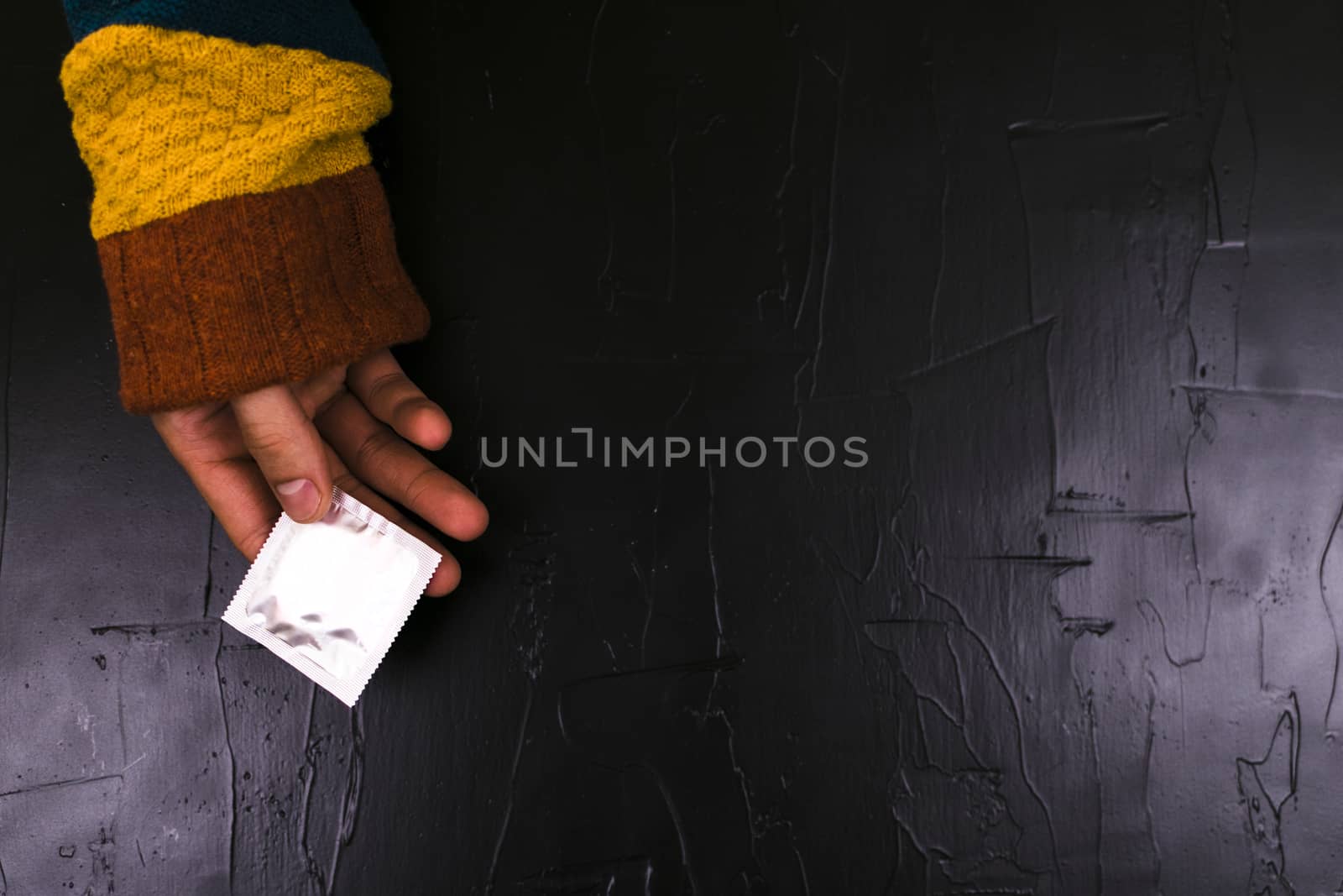 The man reaches for a condom. Black background, the concept of the day of contraceptie