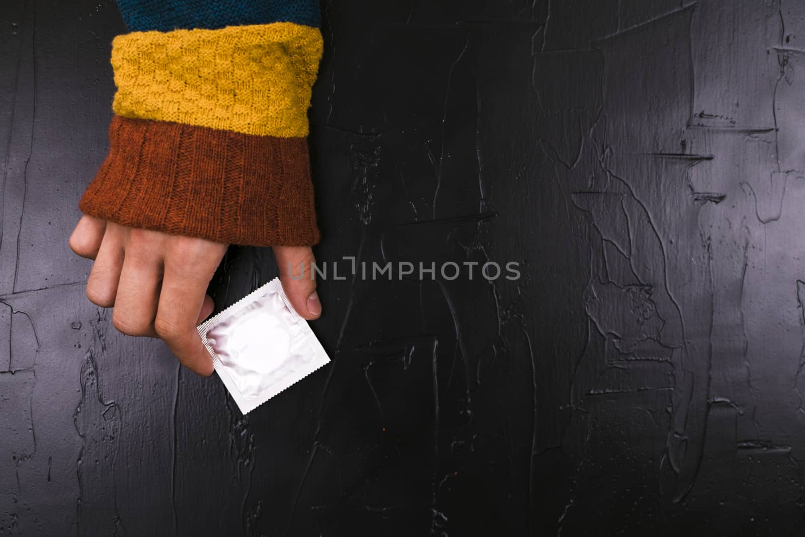 The man reaches for a condom. Black background, the concept of the day of contraceptie