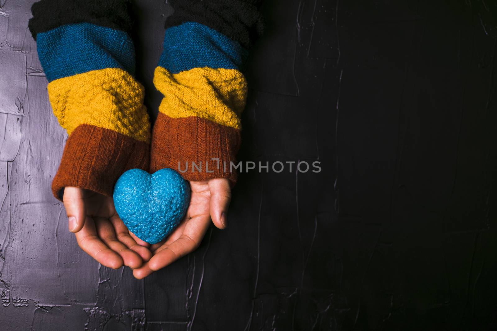 Male hand holds out a blue heart on black background