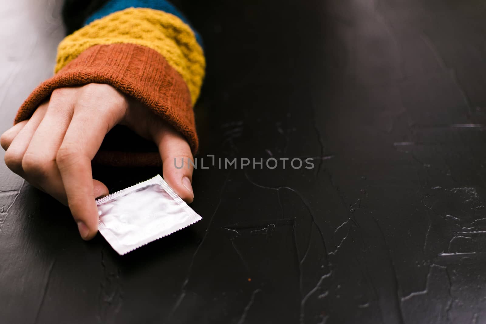 The man reaches for a condom. Black background, the concept of the day of contraceptie