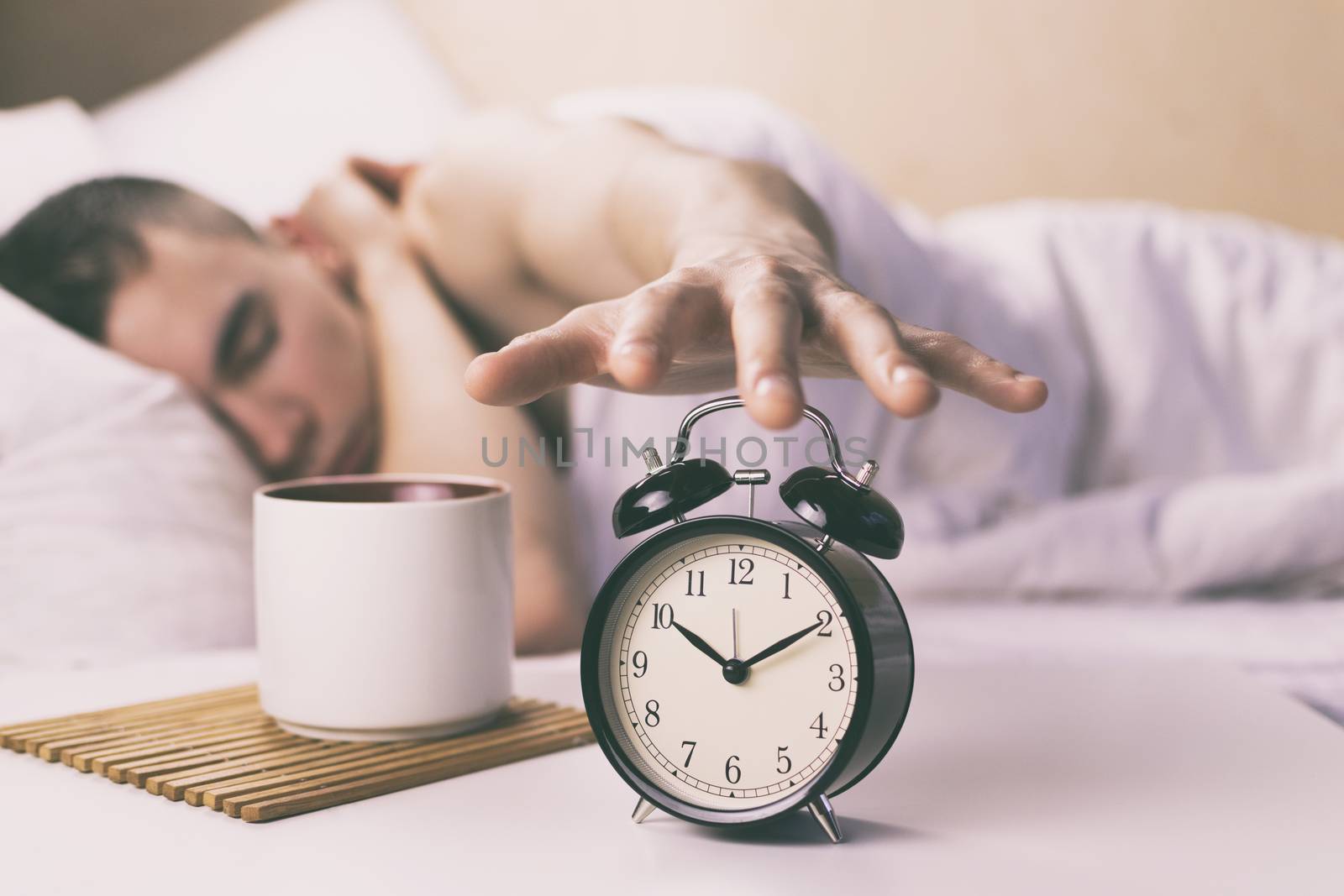 The young man turns off the alarm clock in the morning