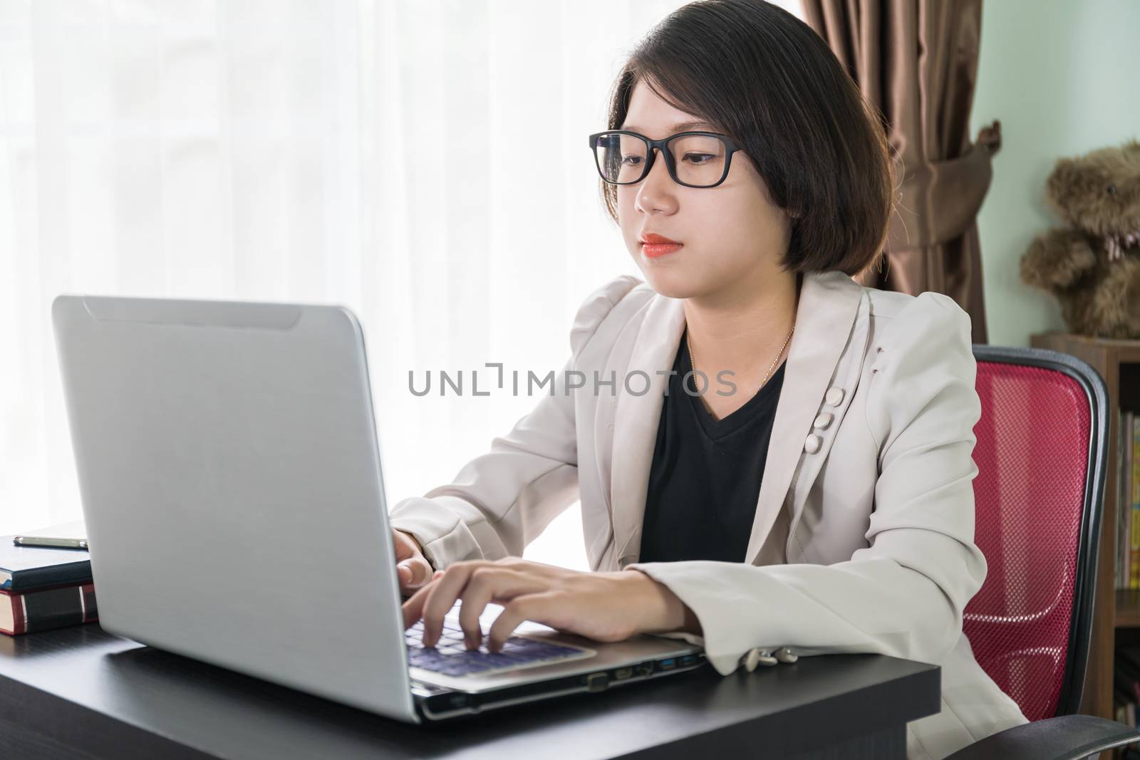 Woman short hair in smart casual wear working on laptop while sitting near window in home office