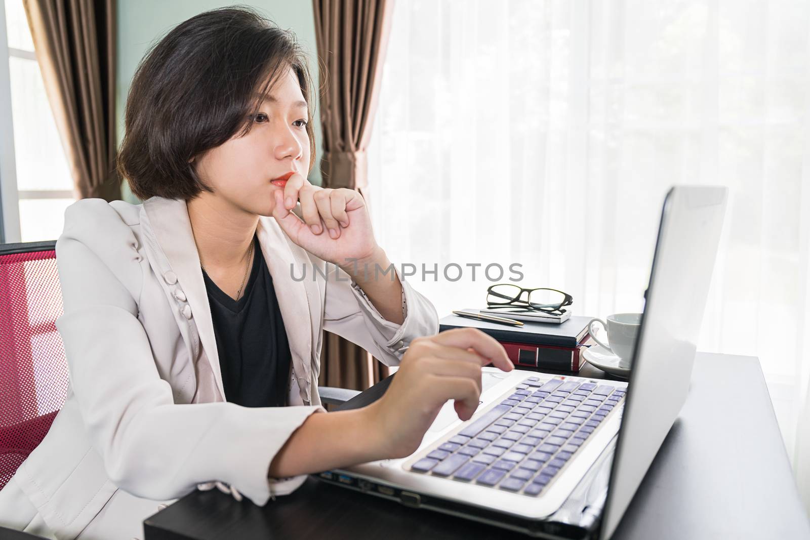 Young asian woman short hair in smart casual wear working on laptop while sitting near window in home office