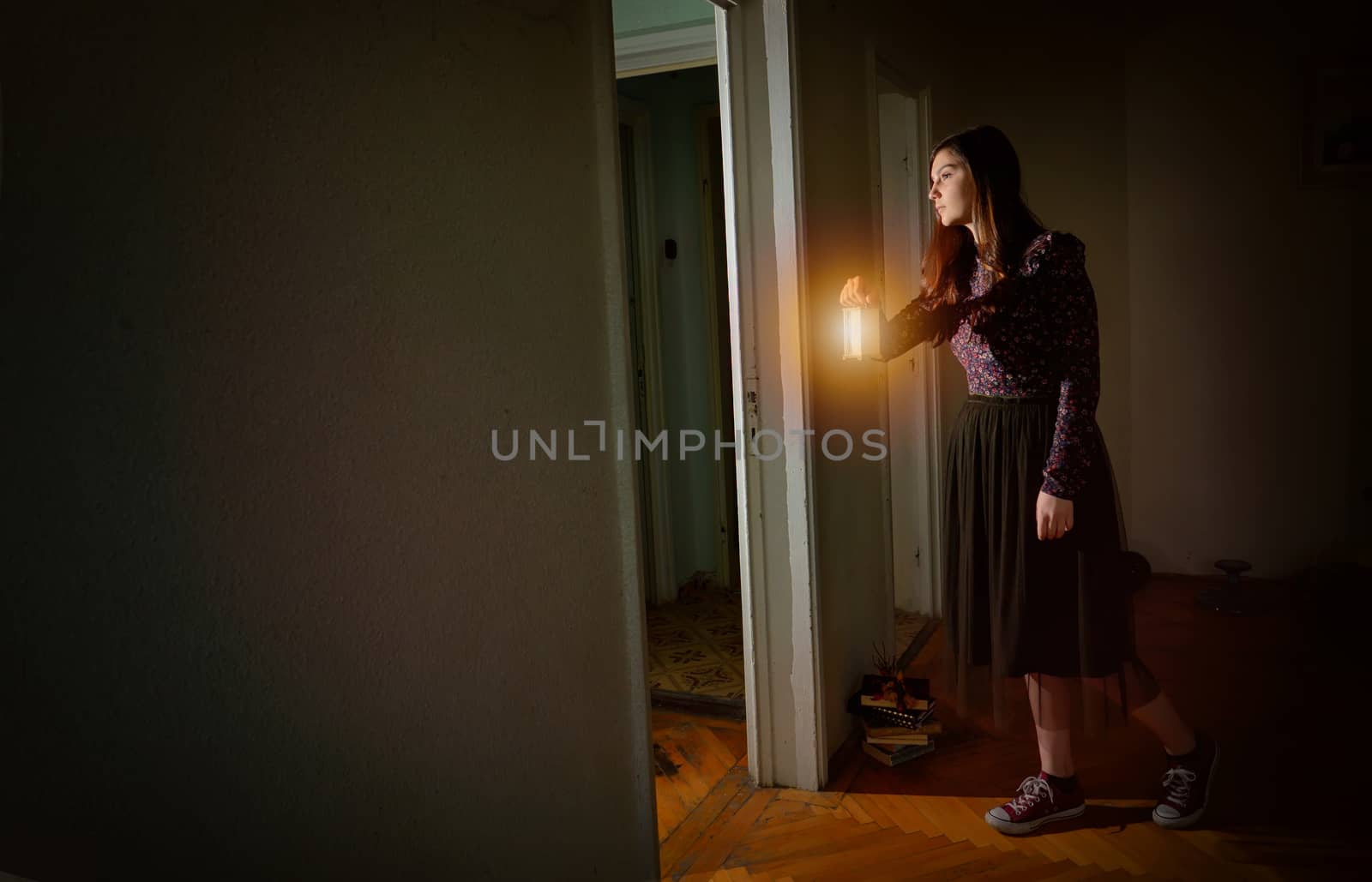 Young girl in black vintage dress with lantern in empty house