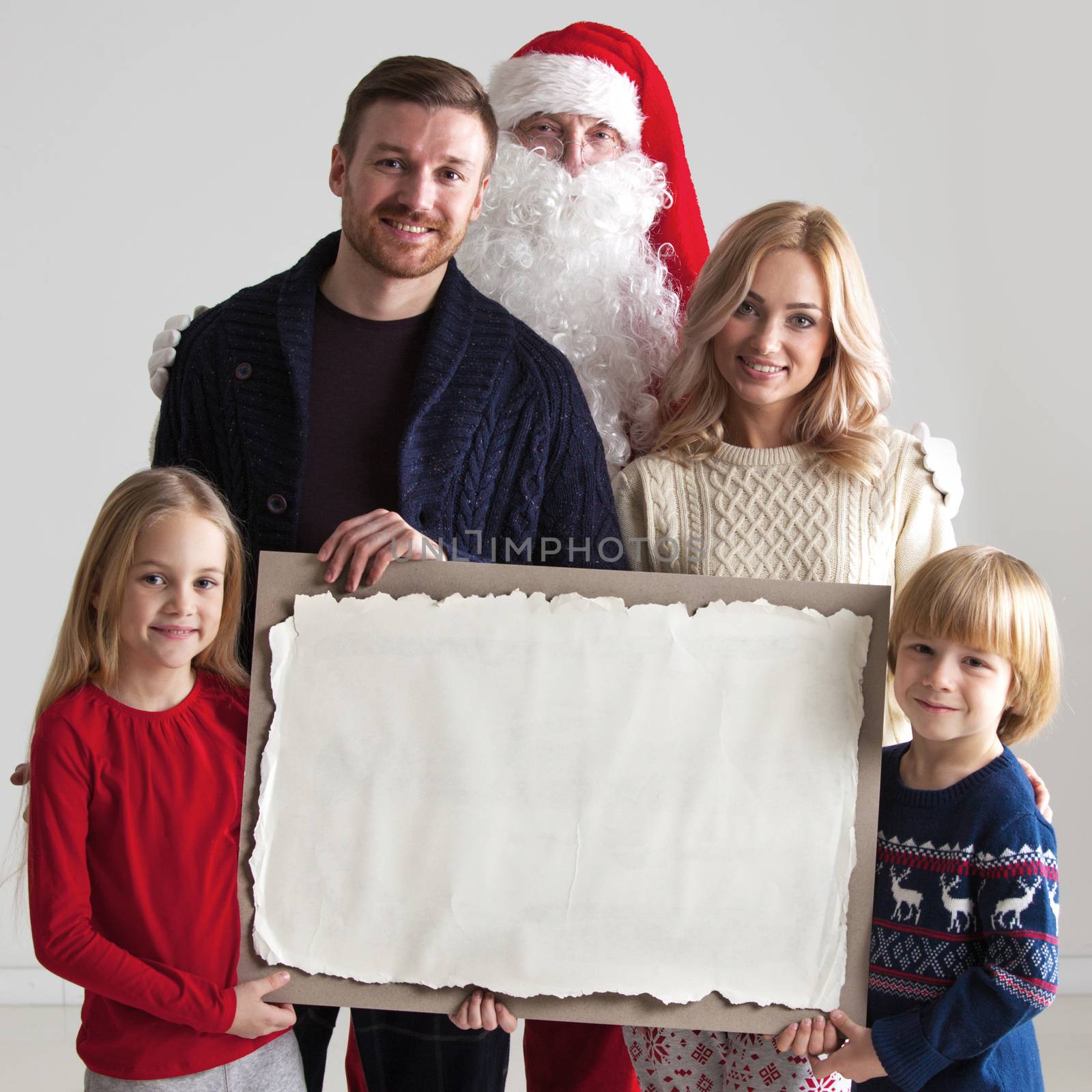 Christmas portrait of happy smiling family with two children and Santa Claus embracing them holding blank vintage paper