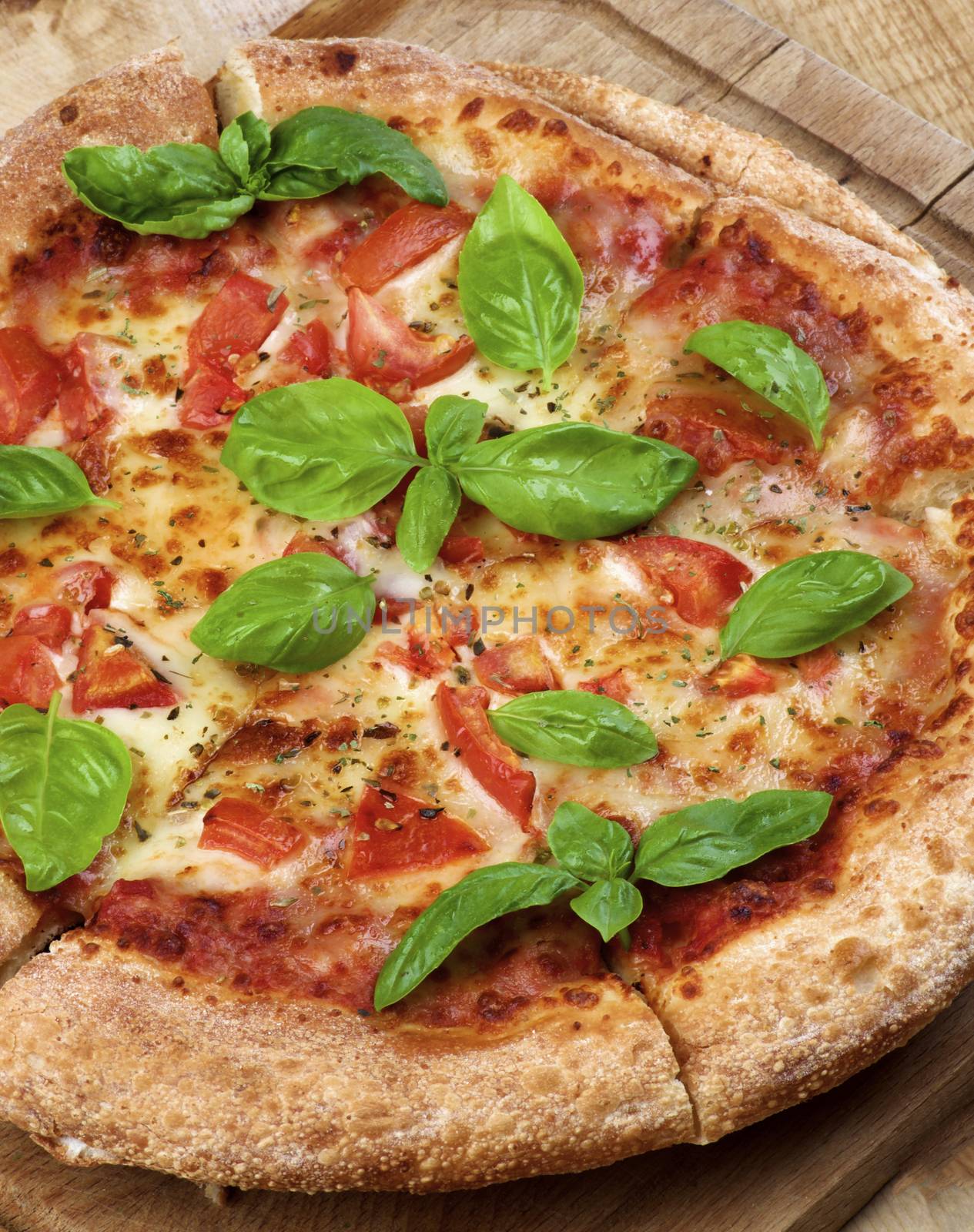 Freshly Baked Margarita Pizza with Tomatoes, Cheese and Basil Leafs on Cutting Board Cross Section on Wooden background