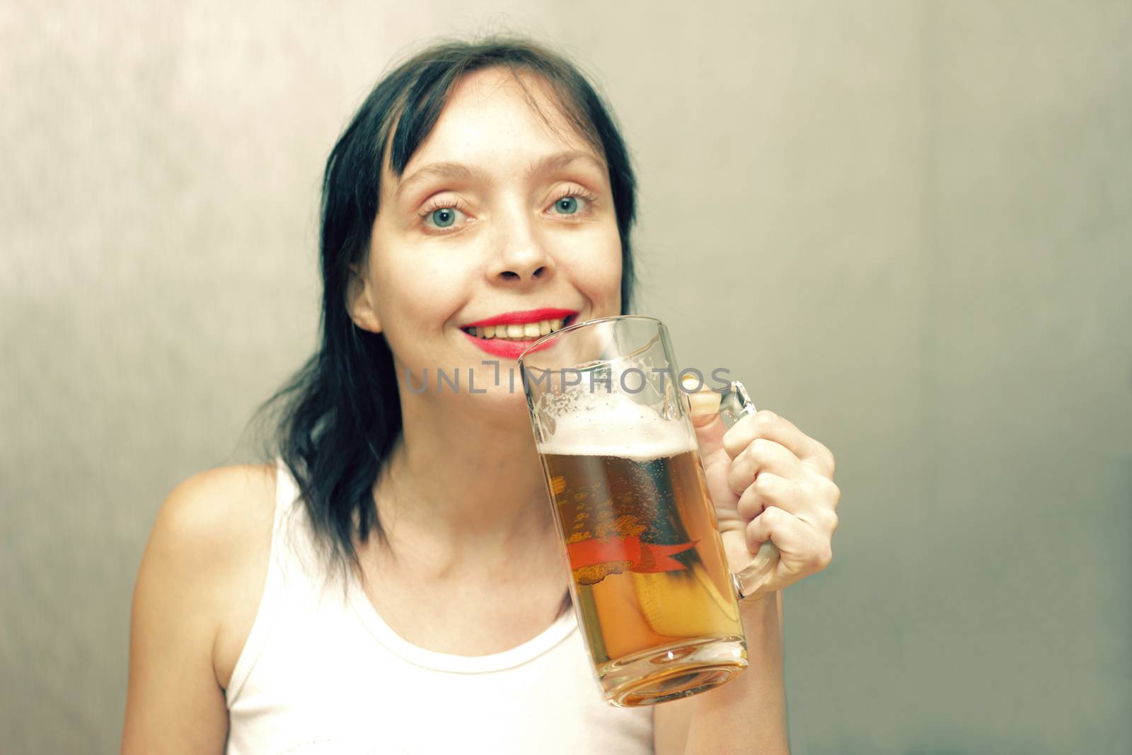 A beautiful woman is drinking beer from a glass beer mug.