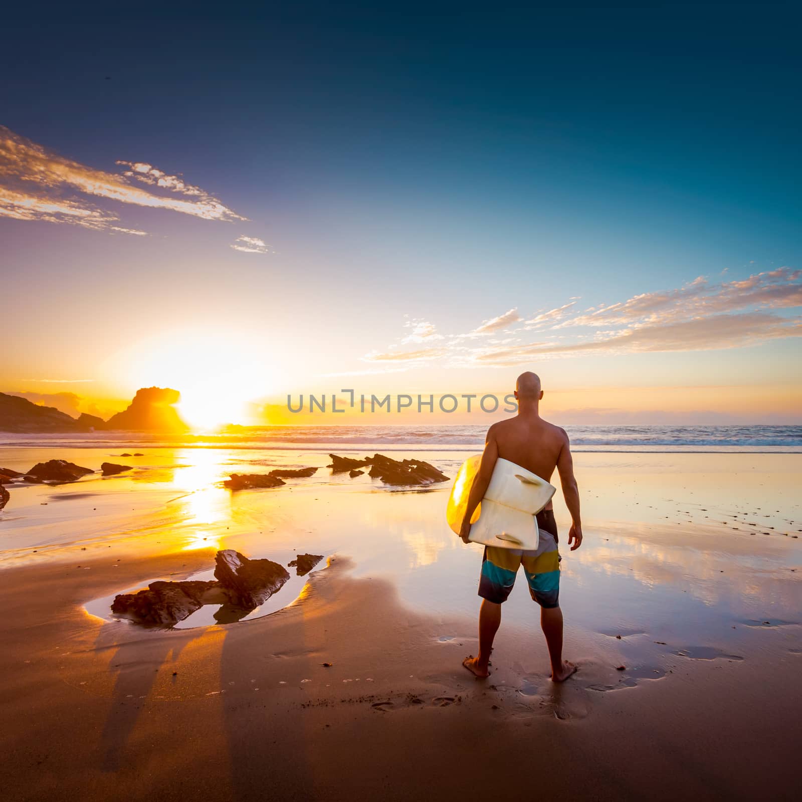 Young man on the beach with his surfboard looking at waves