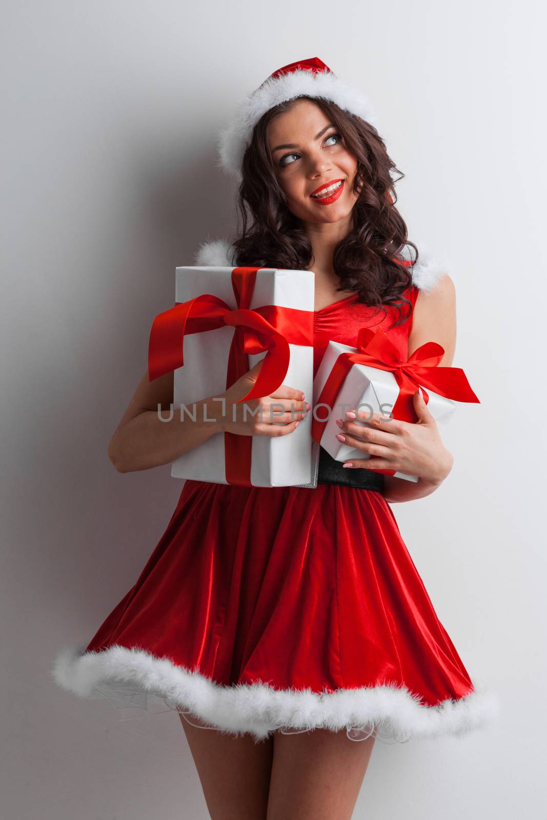 Excited surprised woman in red santa claus outfit holding Christmas presents