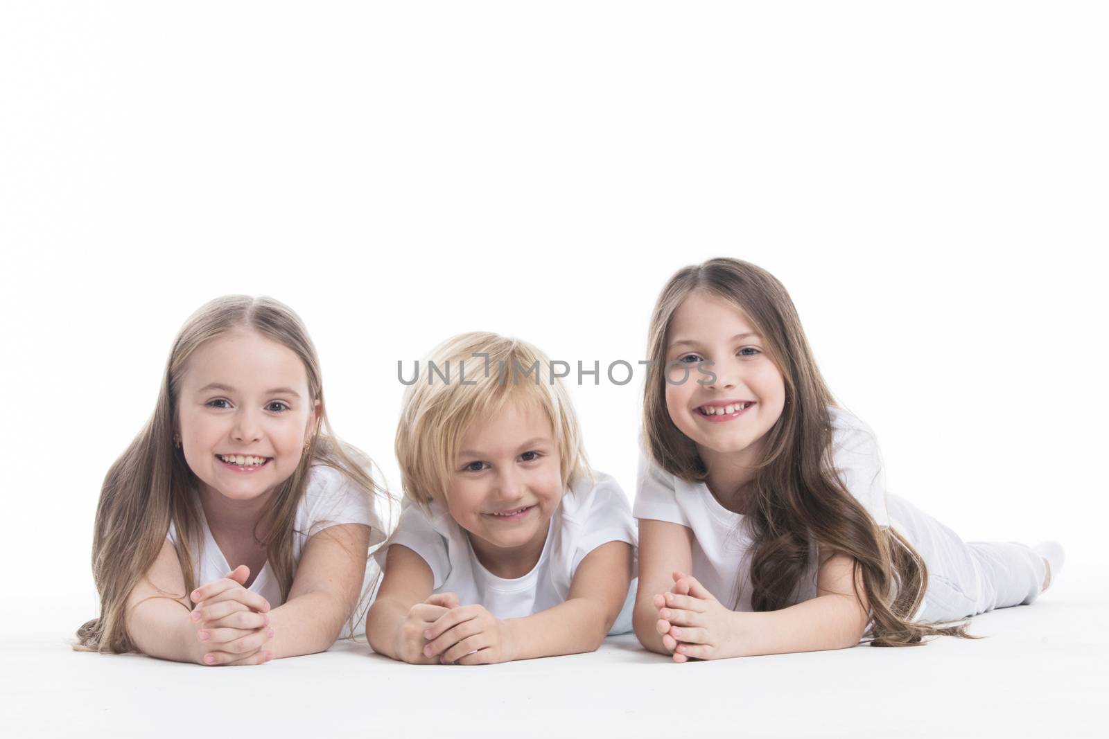 Happy smiling three children in white clothes laying on floor isolated on white background