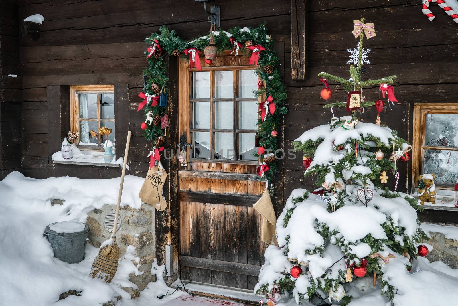 Entrance of a house with Christmas decorations and a Christmas tree covered with snow