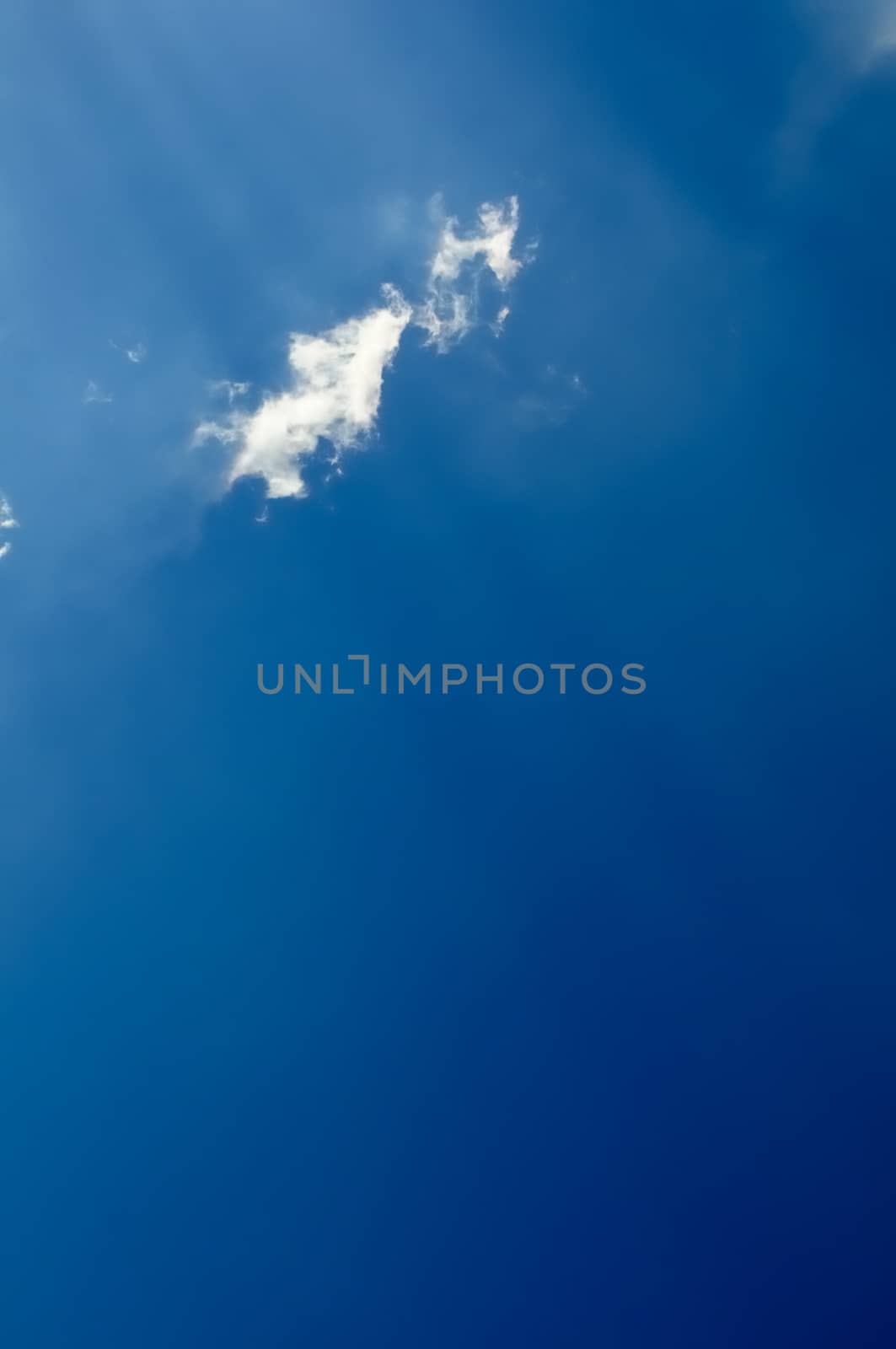 vaste blue sky with sunrays across little fluffy cloud, vertical