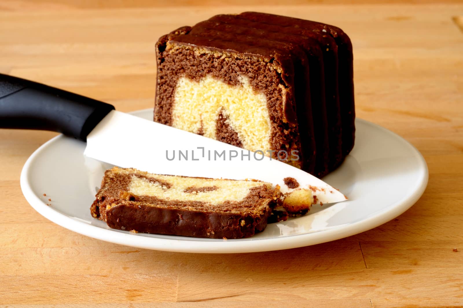 Cutting a slice of delicious chocolate marbled cake, with a white ceramic knife