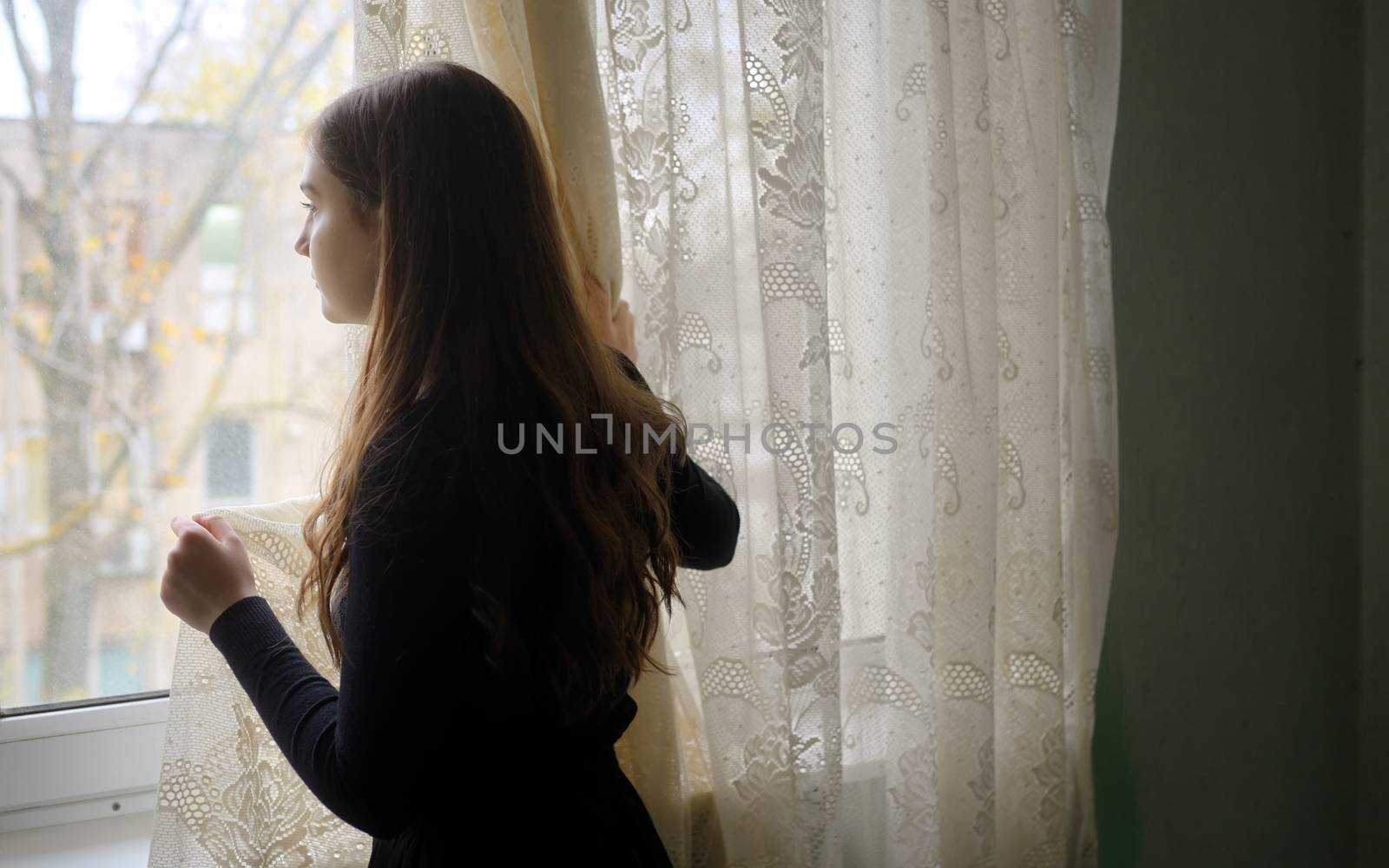 Young girl in black vintage dress standing near window 