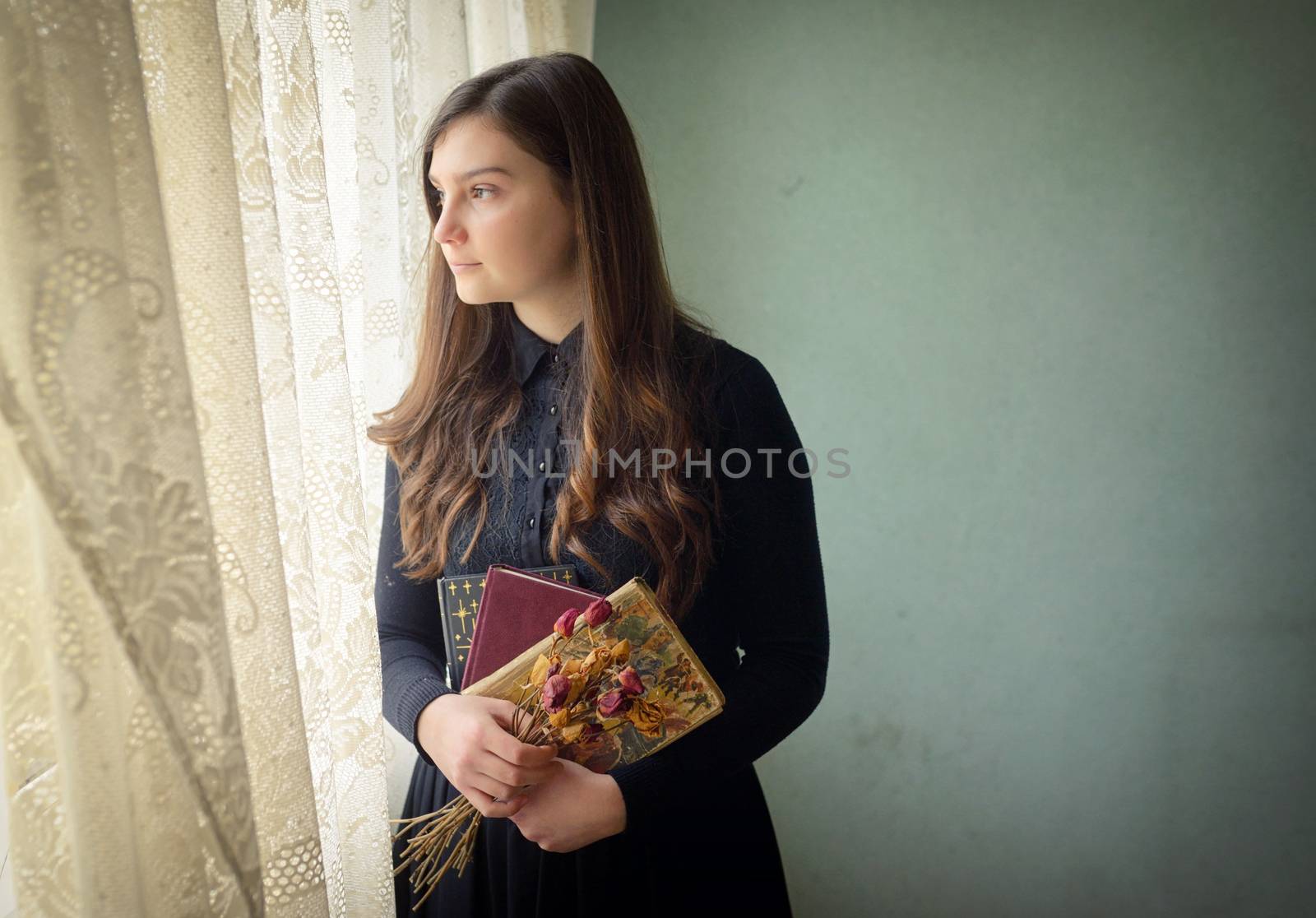 Young girl in black vintage dress standing near window 