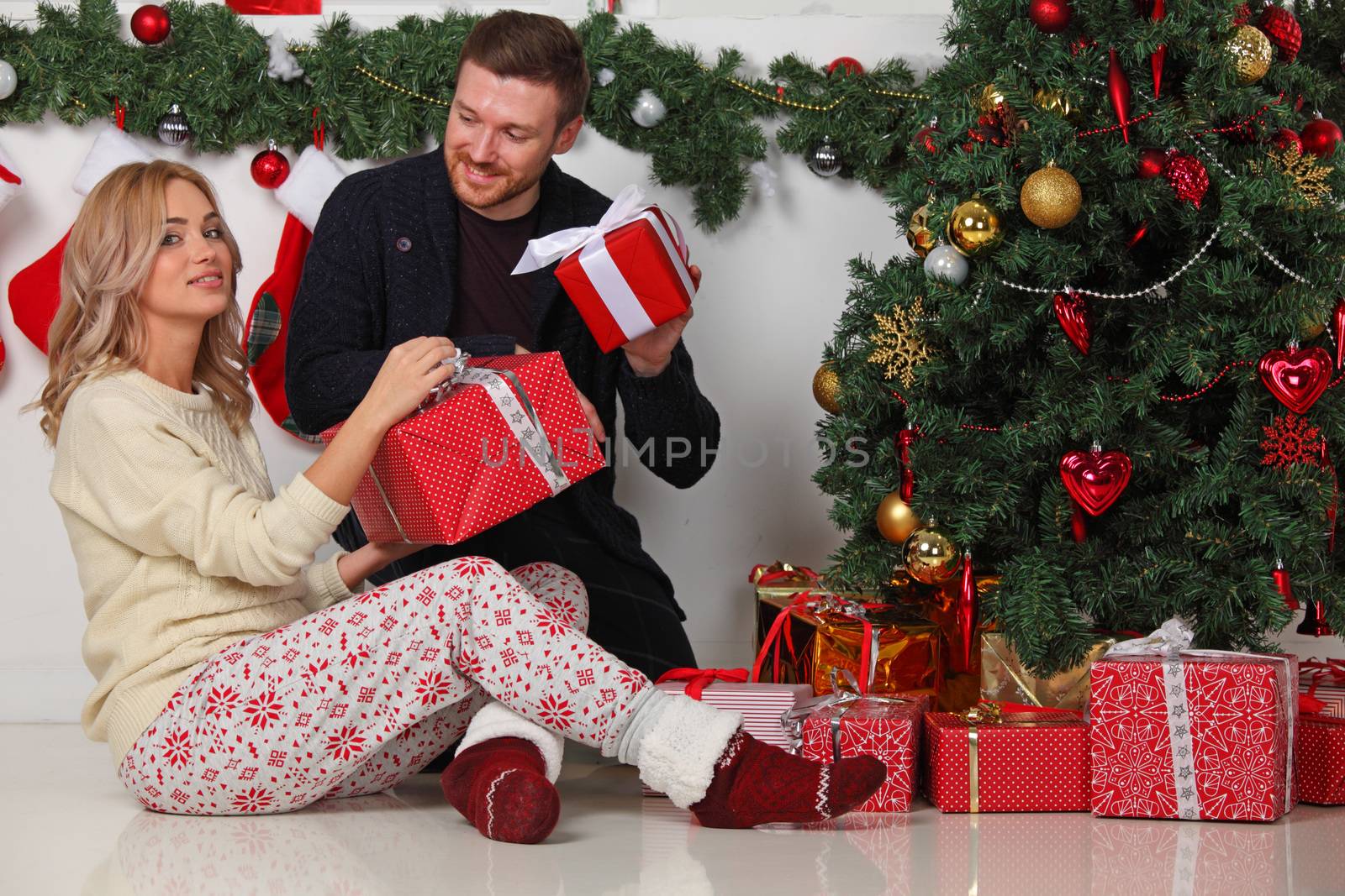 Couple in love sitting next to a nicely decorated Christmas tree, hloding Christmas gifts and smiling