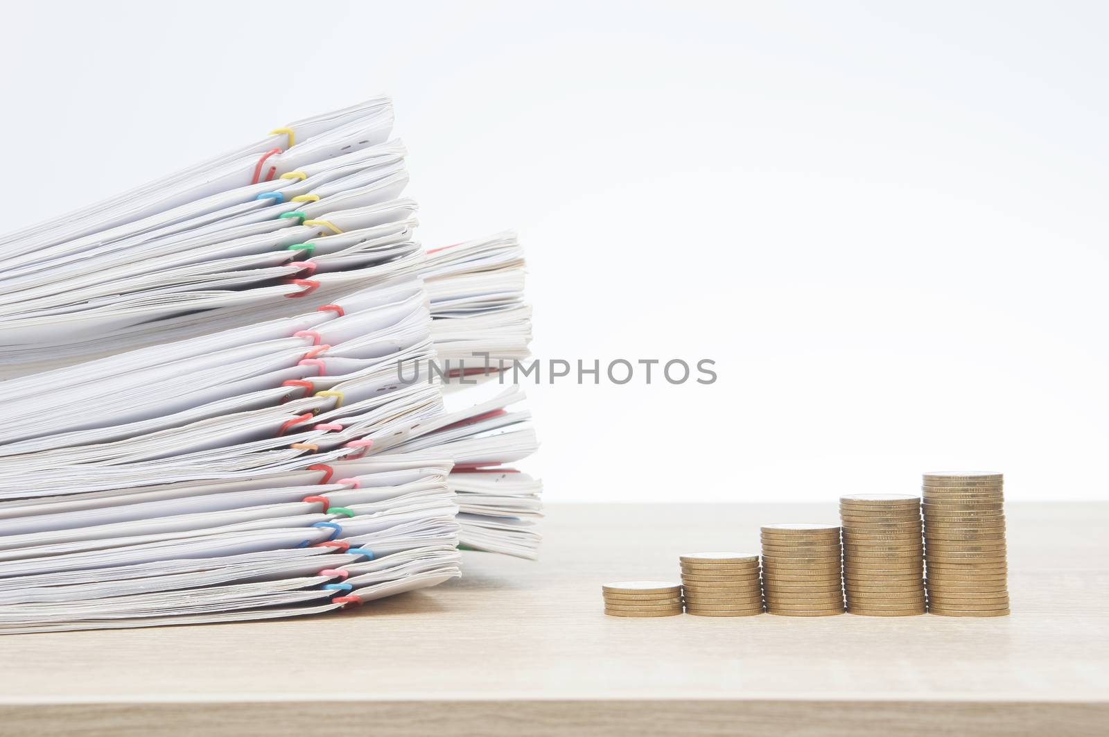 Step pile of gold coins and overload report of sale and receipt with colorful paper clip on wooden table with white background and copy space. Business and finance concept rich and successful photo.